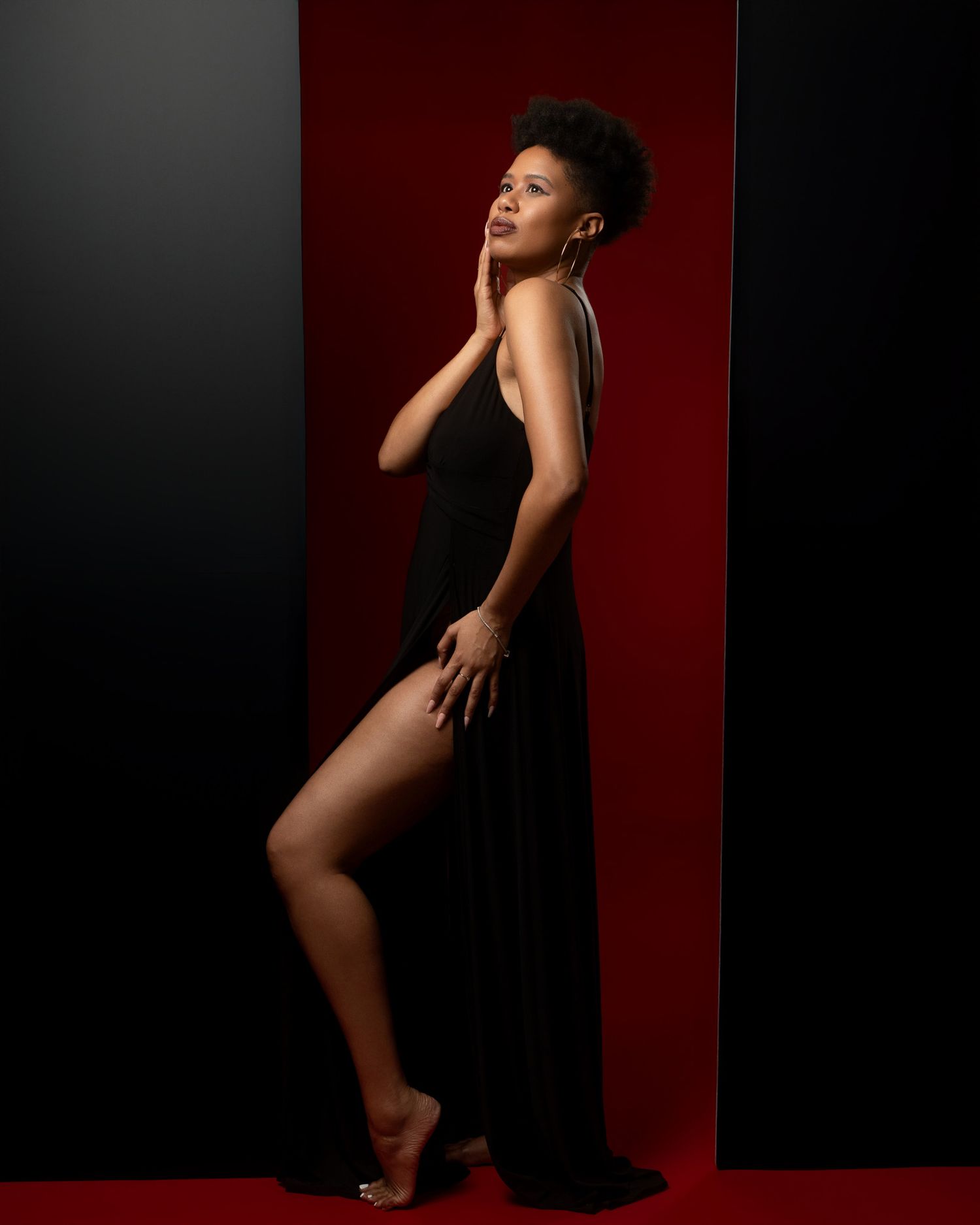 Graceful dance-inspired pose in black dress against dramatic red and black background.