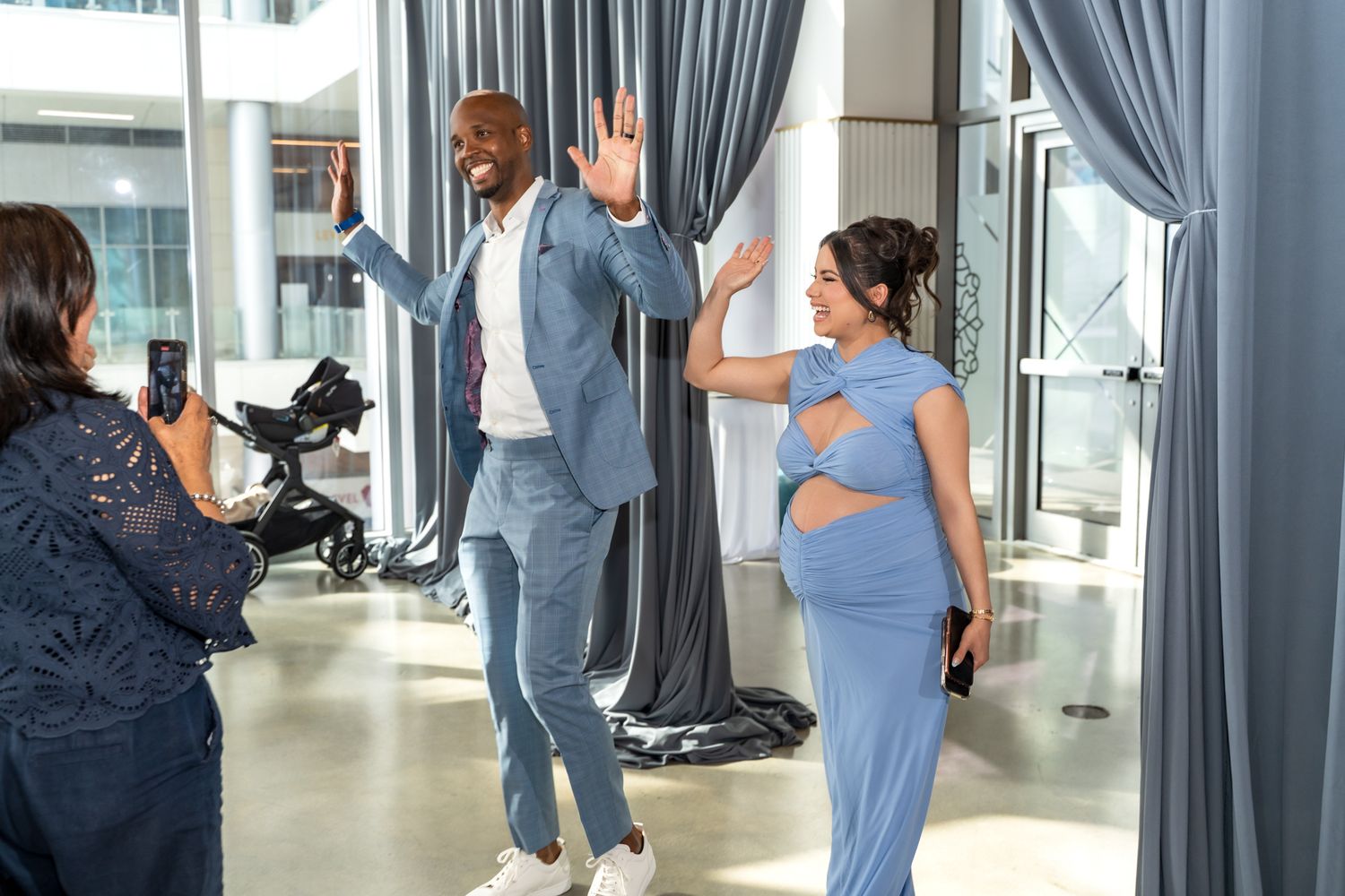 Candid photo of couple waving during baby shower celebration with elegant decor.