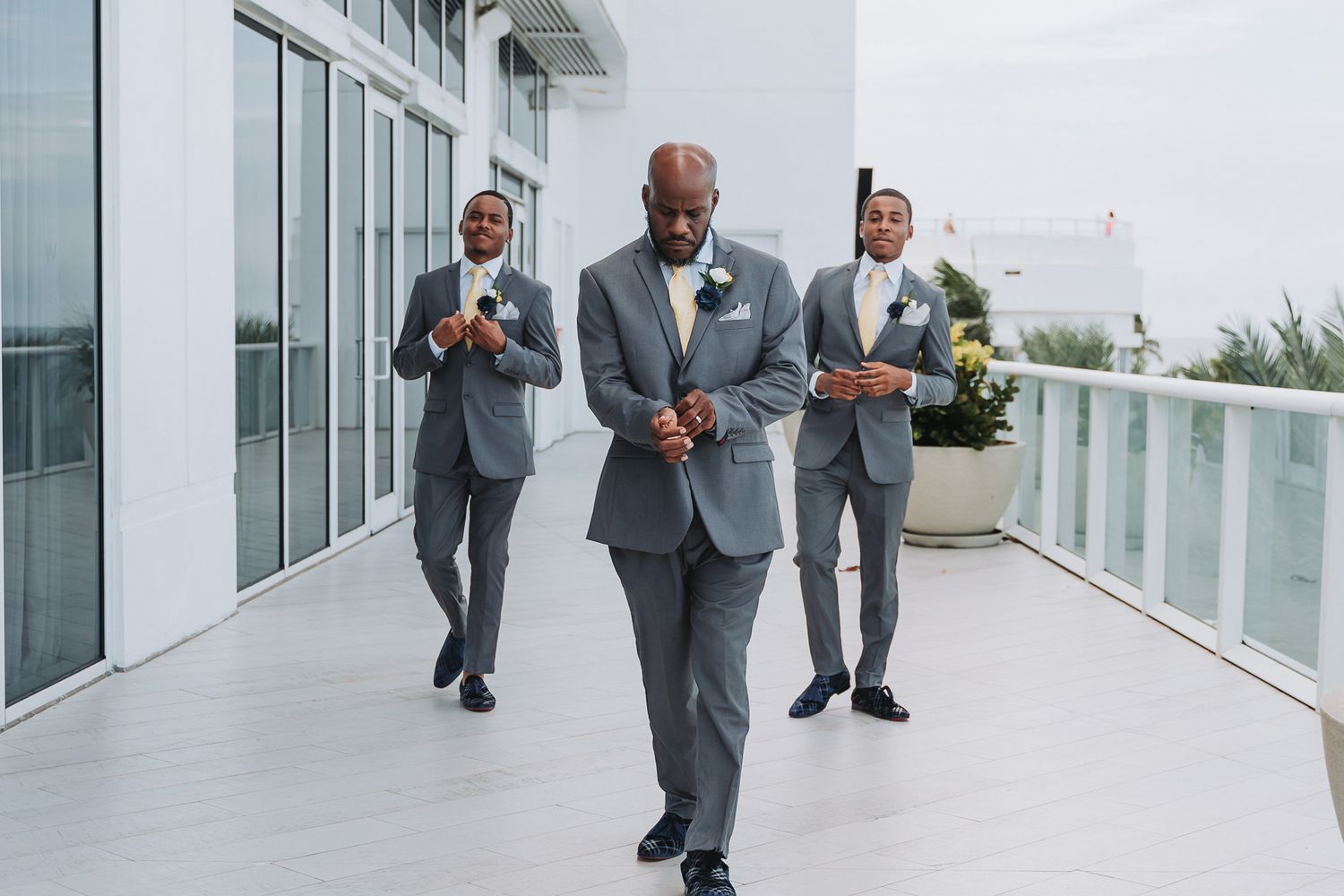 Groom and groomsmen walking on outdoor terrace in grey suits.