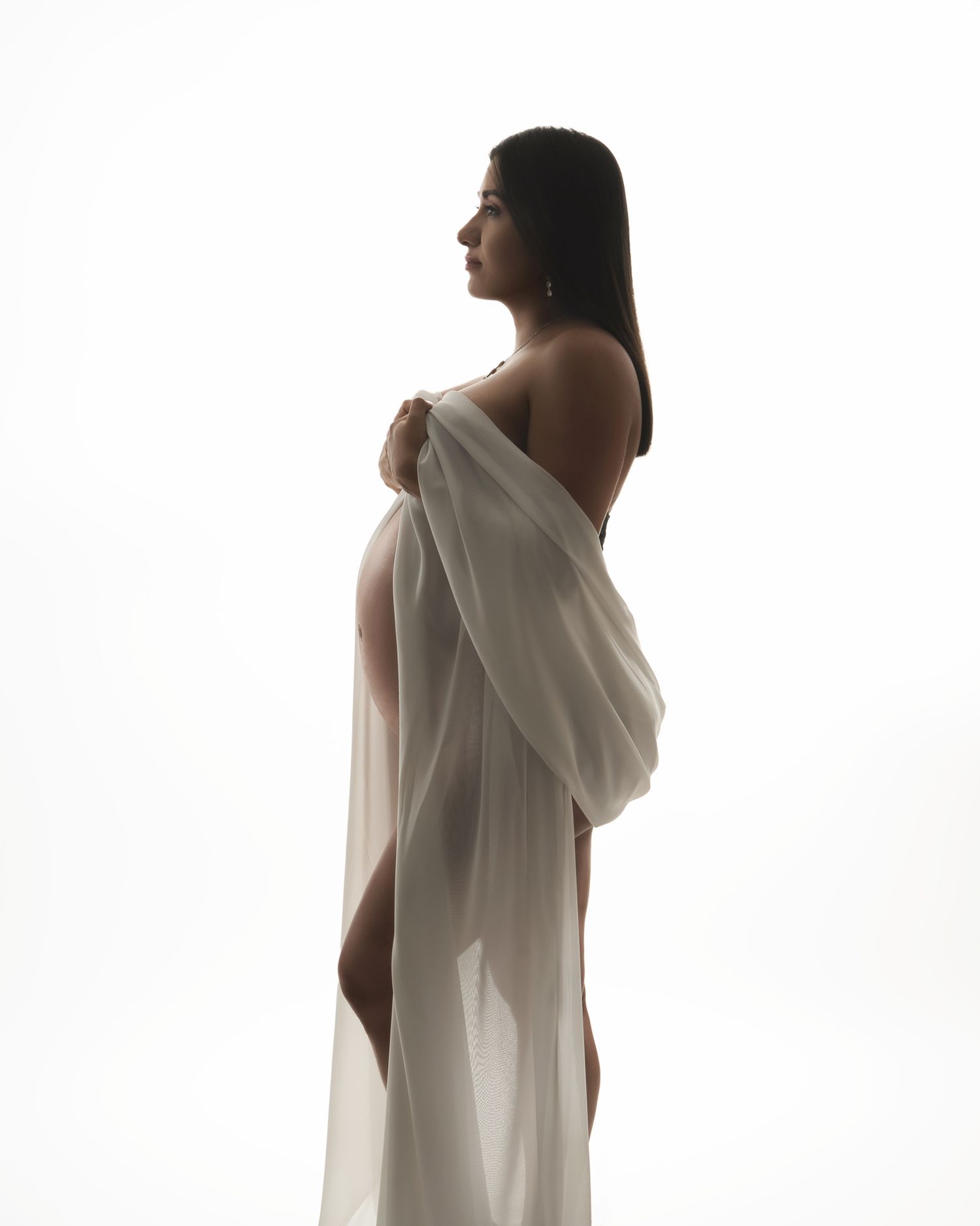 Figure in flowing white fabric poses artistically against bright background in minimalist studio setting.