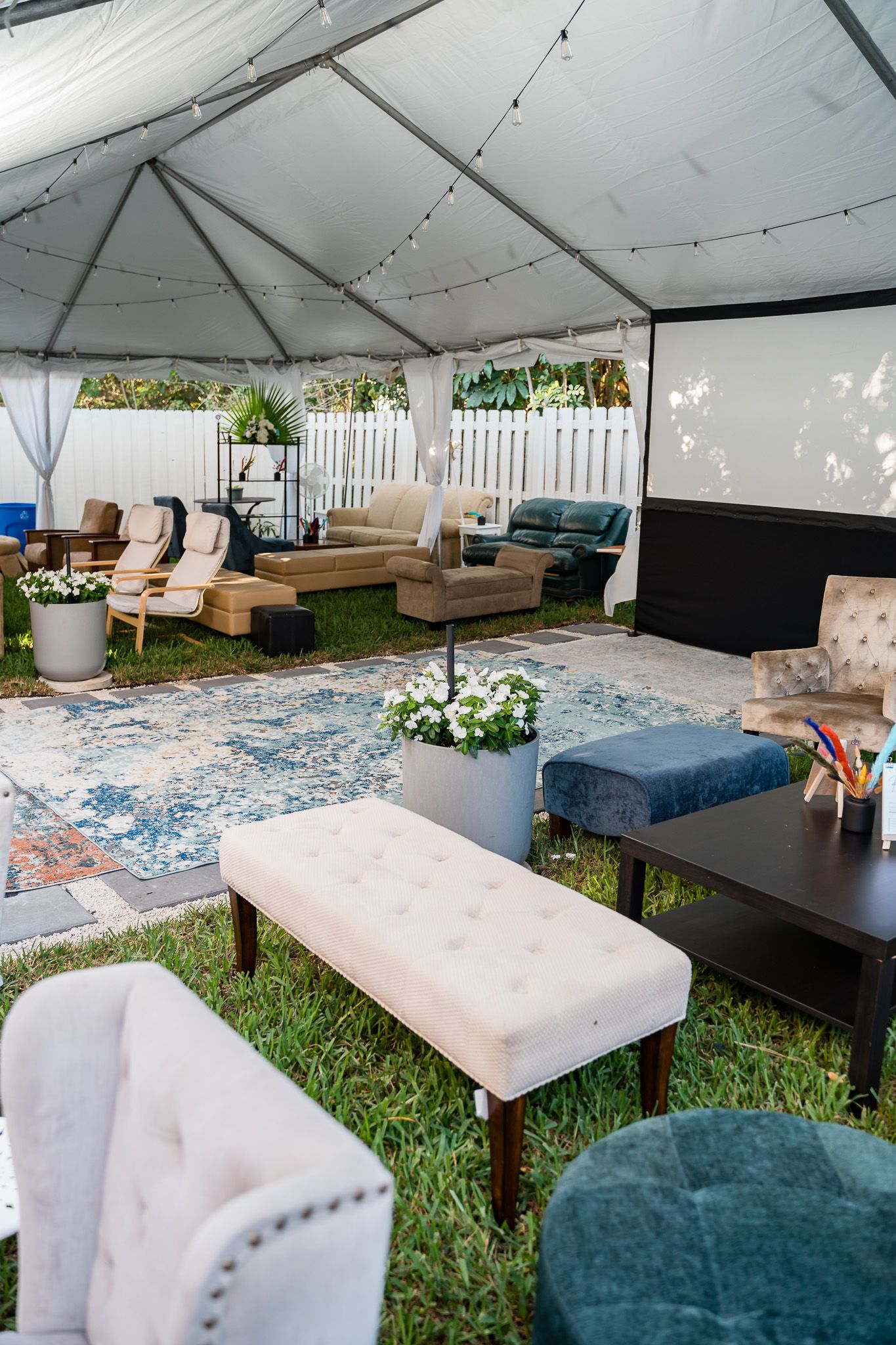 Elegant outdoor lounge area under white tent with mixed seating and blue area rug.