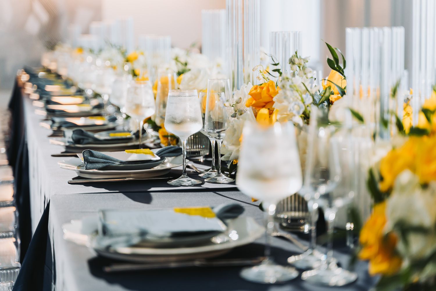 Wedding reception table with black charger plates and yellow floral arrangements.