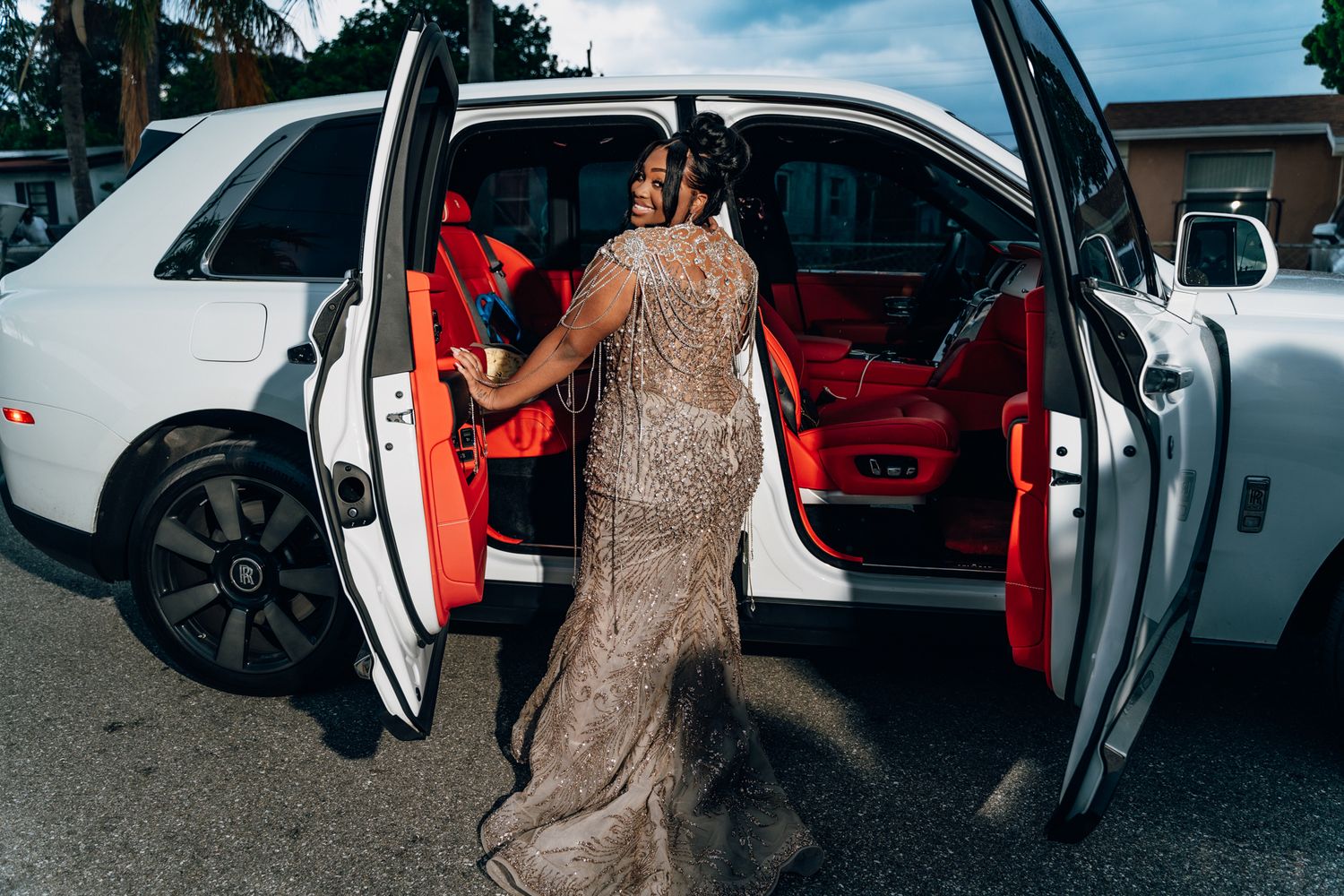 A luxurious beaded evening gown shown next to a white Rolls Royce with red interior.