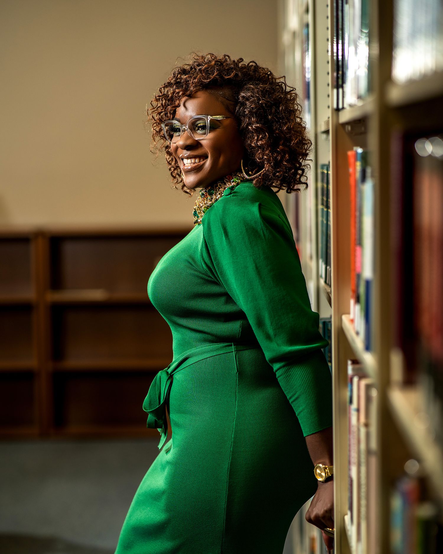 Portrait of someone in an emerald green dress posing by library shelves.
