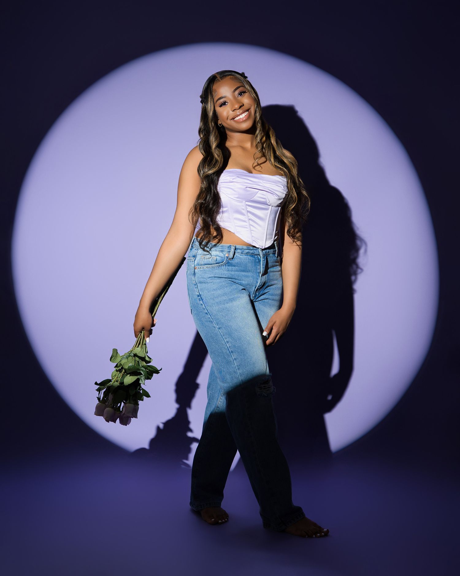 Stylish portrait against purple backdrop featuring casual outfit and held greenery.