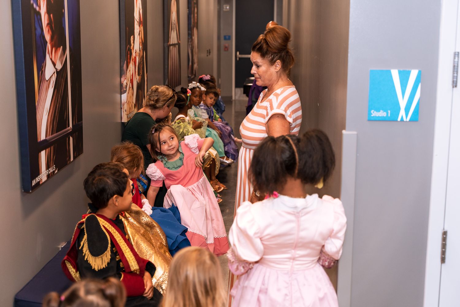 Group of children in dress-up costumes lined up in a hallway at an event.