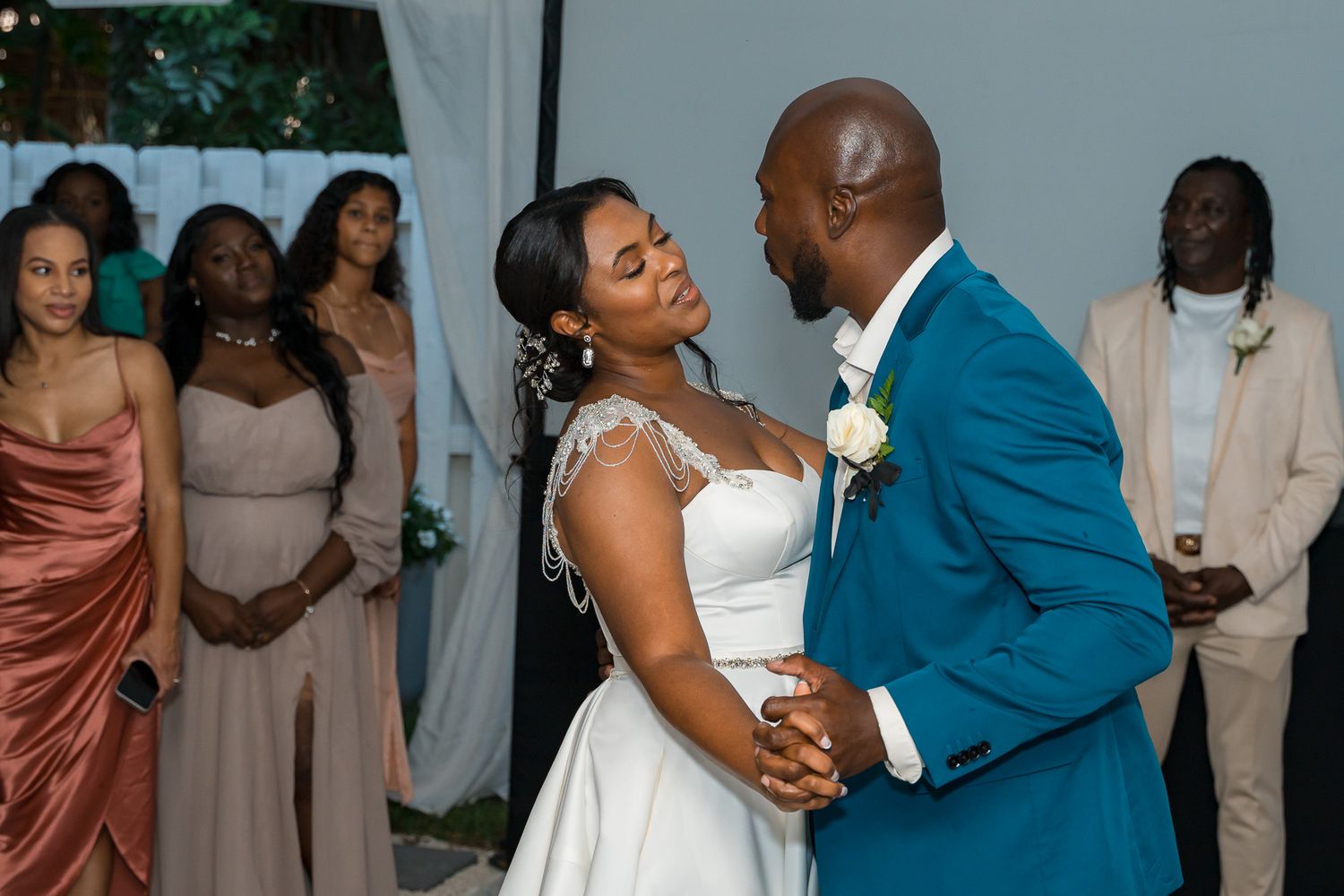 Couple shares intimate dance moment at wedding reception surrounded by guests in formal attire.