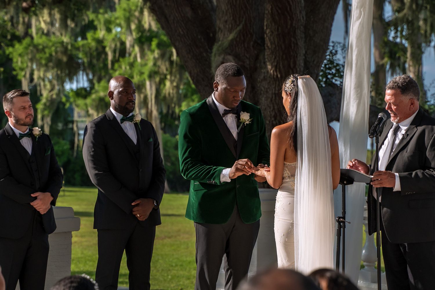 Outdoor wedding ceremony under Spanish moss trees with a couple exchanging vows at the altar.