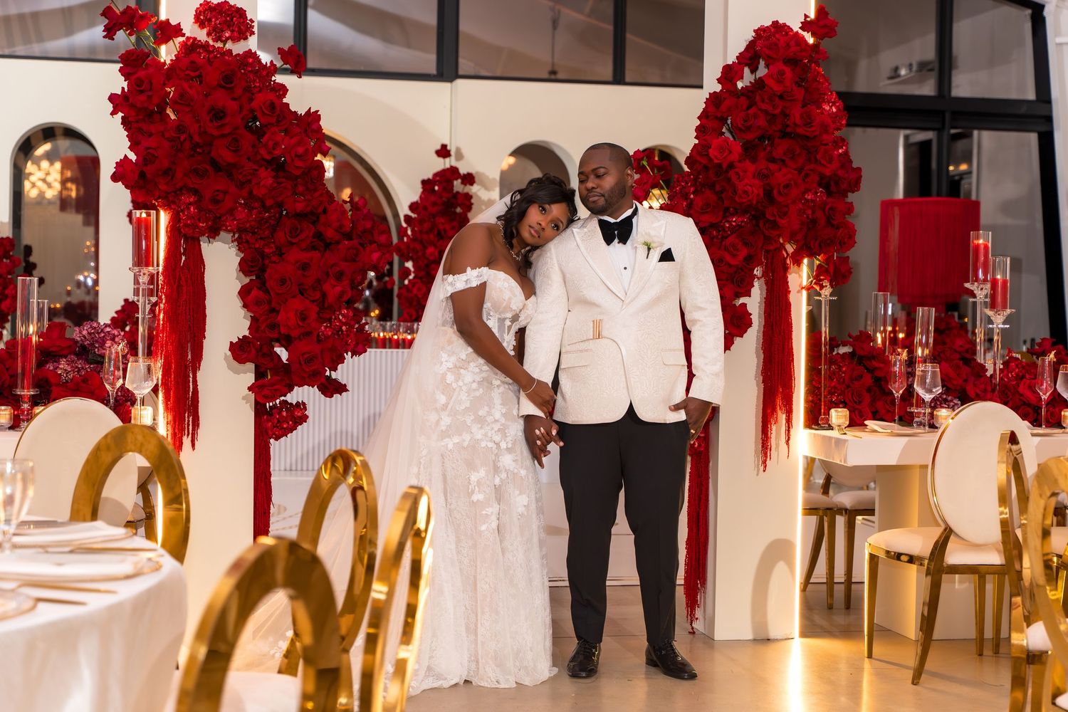 Elegant wedding reception space decorated with dramatic red floral arrangements and gold accents.