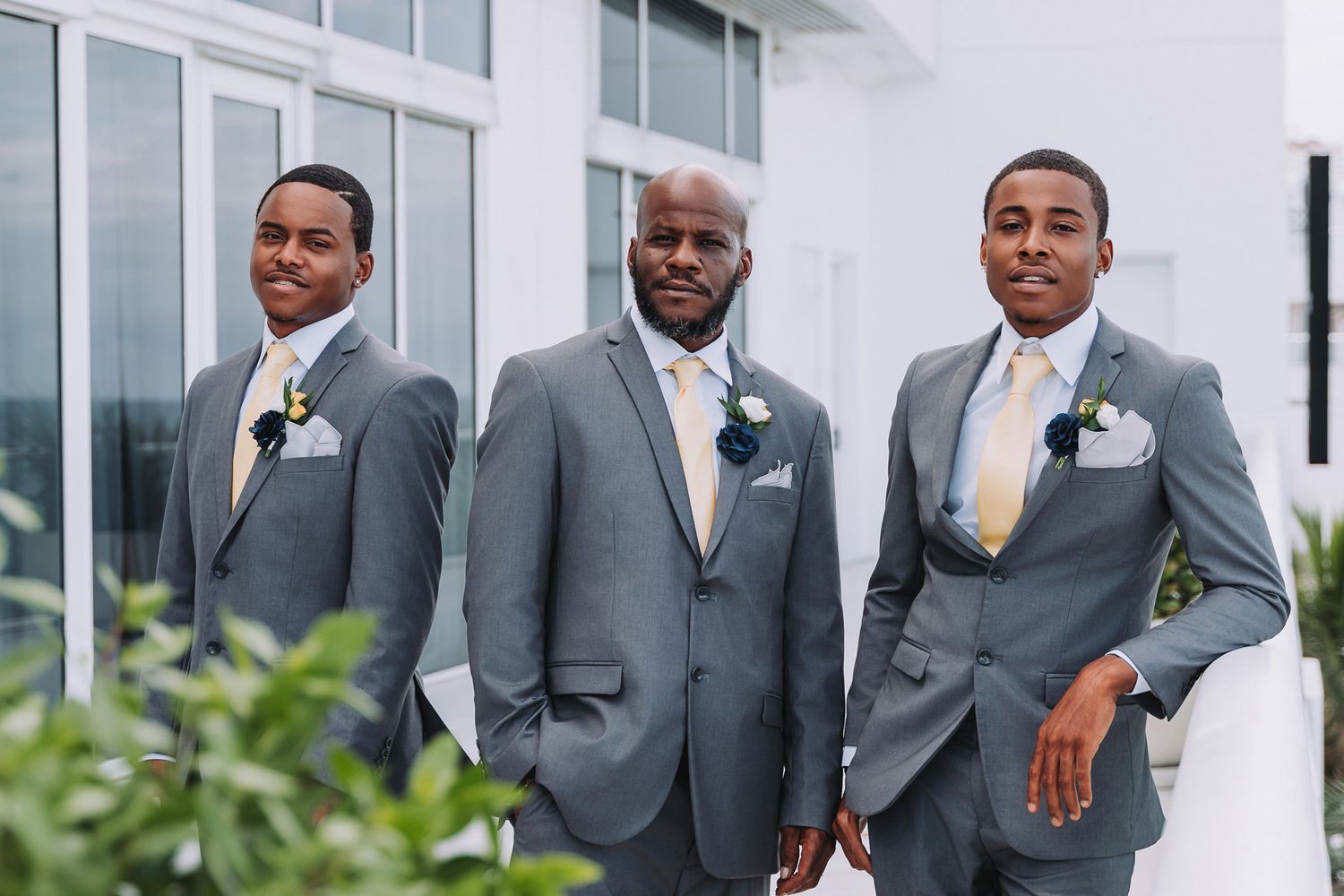 Groomsmen in matching grey suits with boutonnieres pose outdoors for wedding portrait.