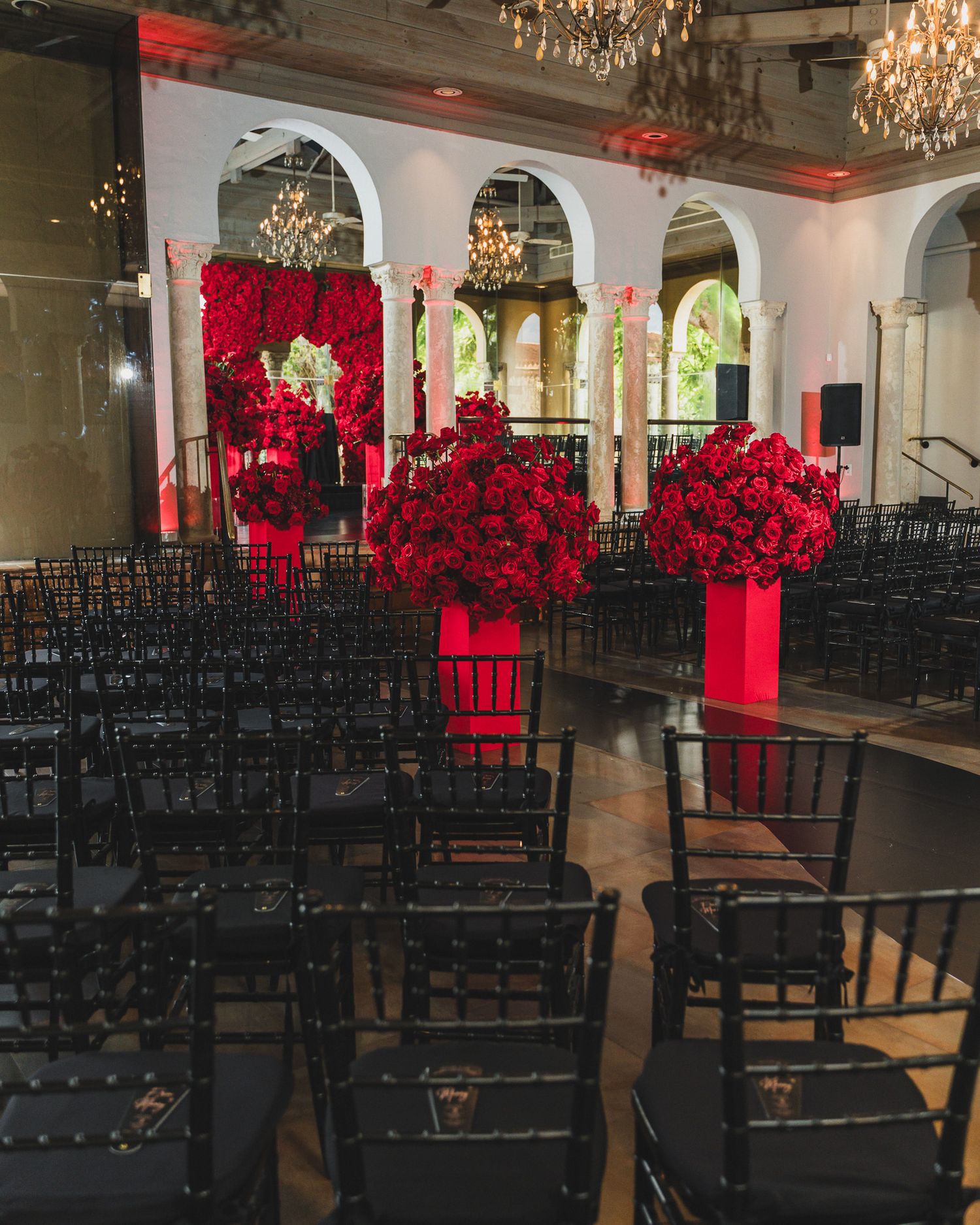 Wedding ceremony space with black chairs and stunning red floral arrangements on pedestals.