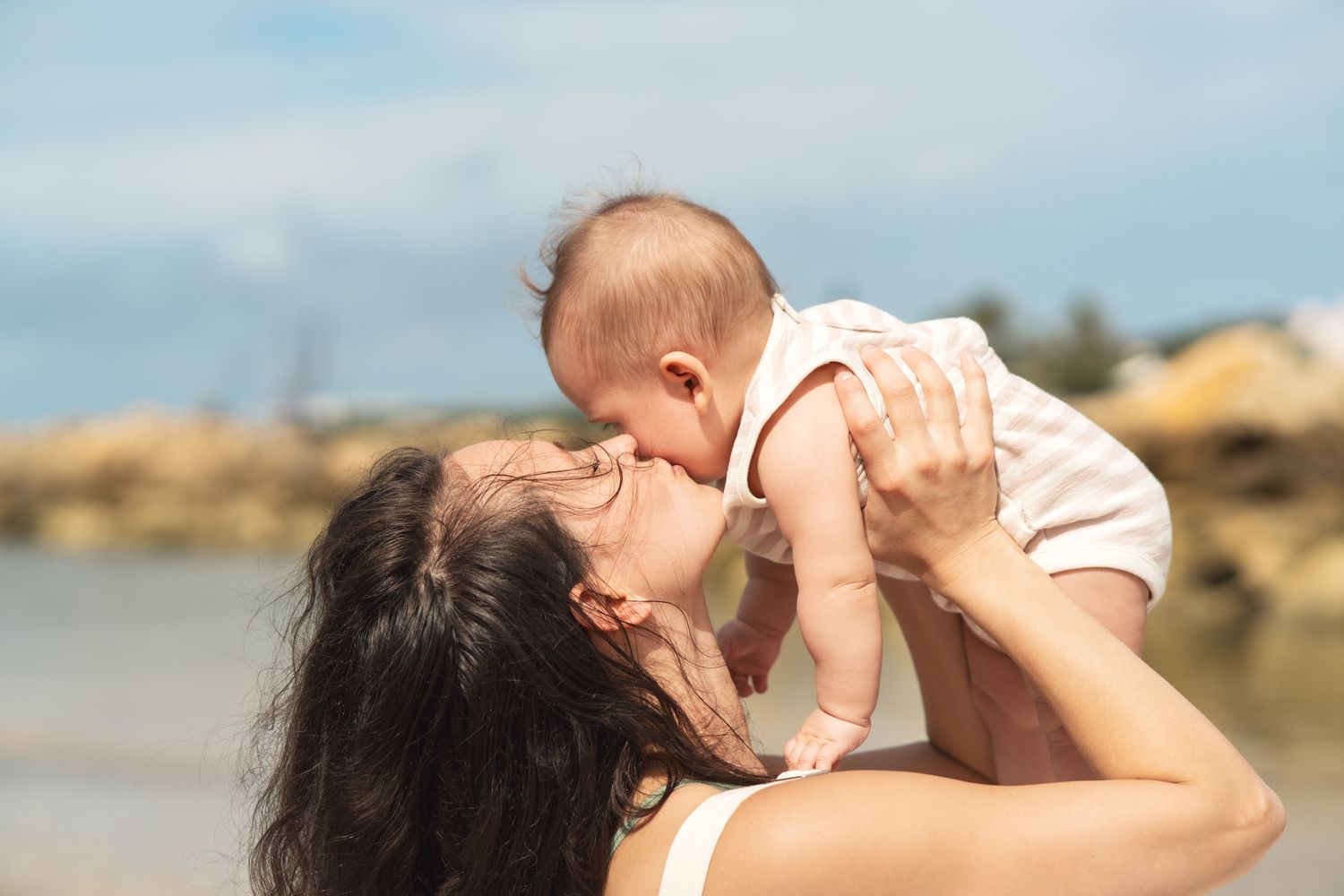 A tender moment between parent and baby as they play together on a rocky beach.