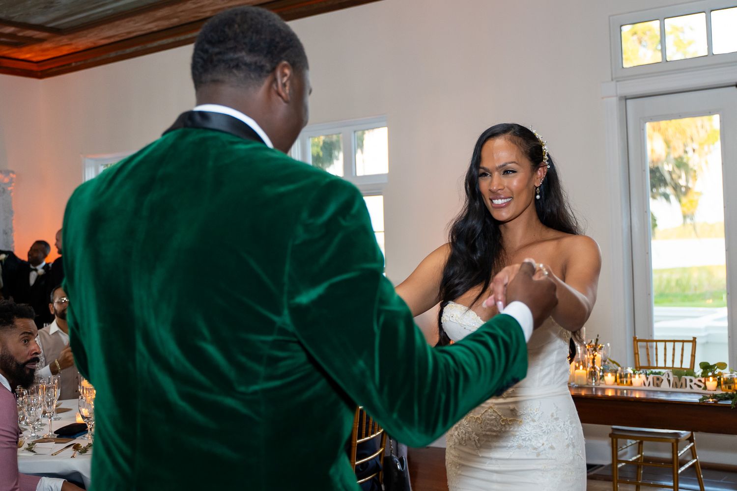 Couple dancing together at reception venue with guests in background.