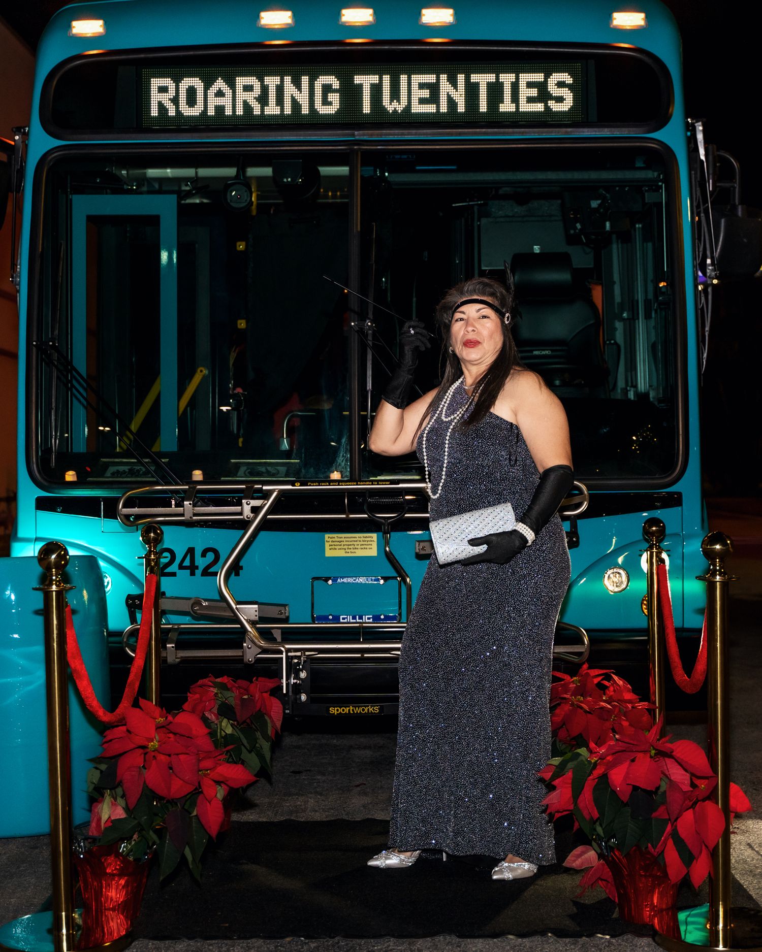 A guest in a sparkly dress poses in front of a turquoise bus labeled 'Roaring Twenties'.