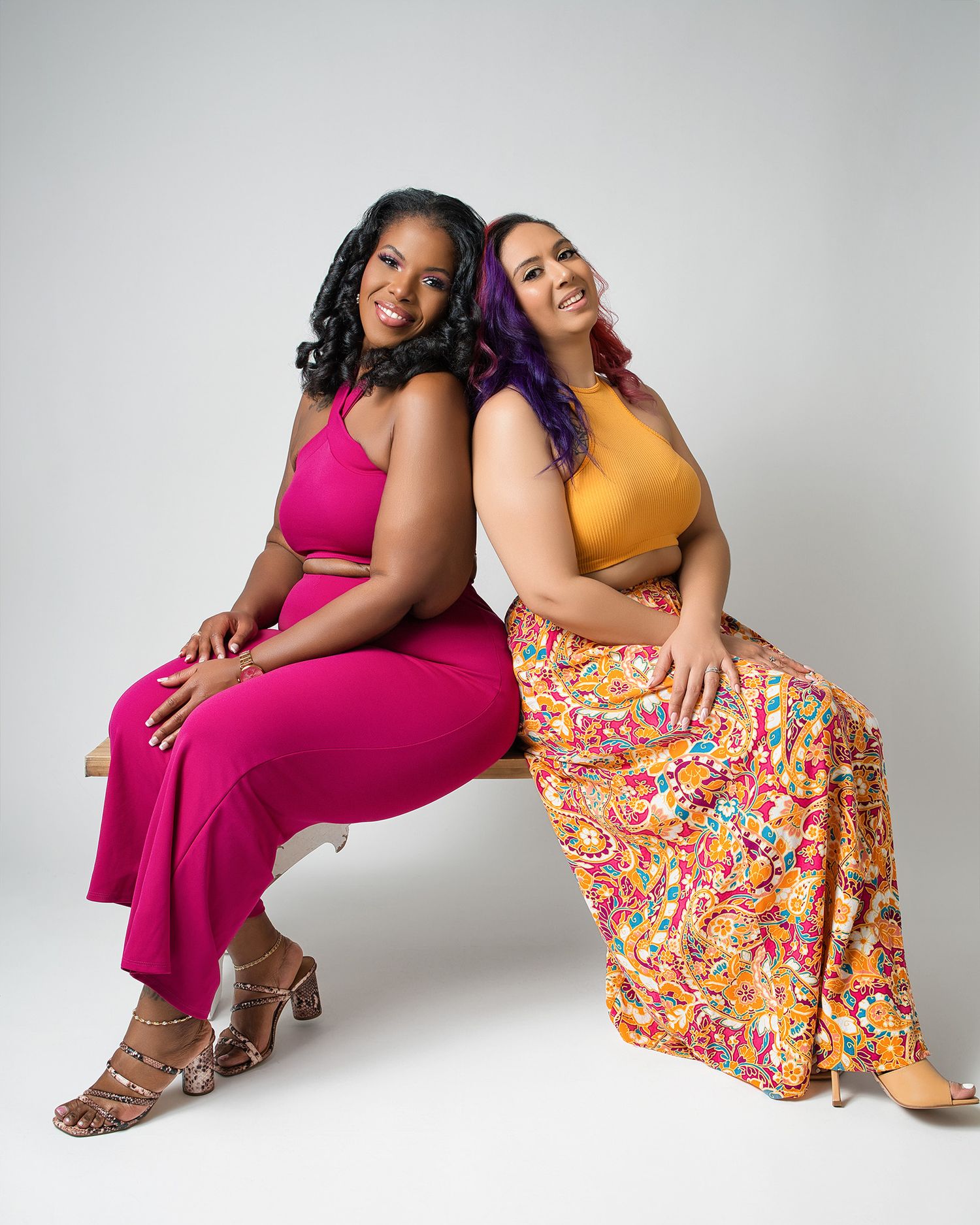 Models wearing pink and yellow outfits pose on white backdrop for fashion photography.