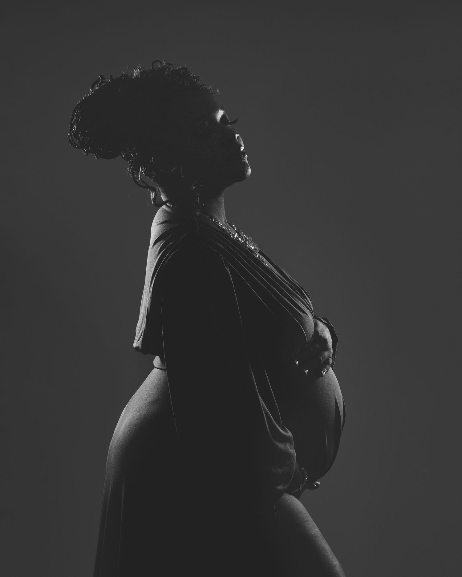 Dramatic black and white silhouette maternity portrait showing a side profile pose.