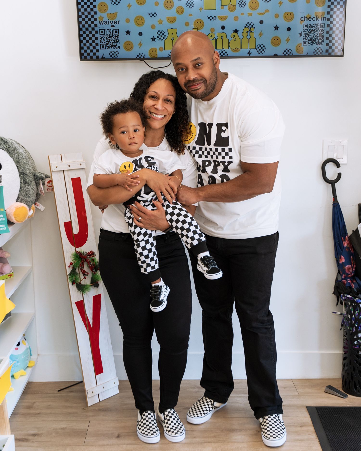 Family wearing matching black and white checkered outfits posing against decorated party wall.