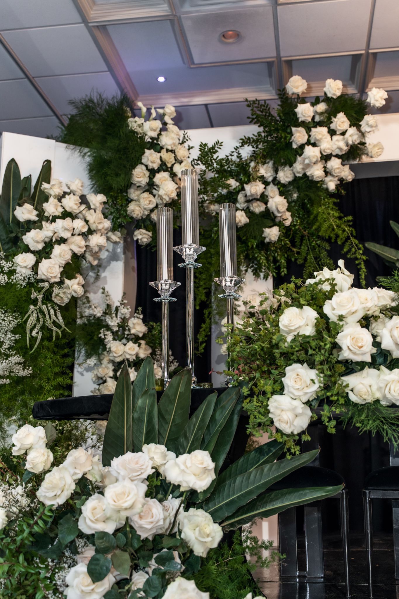 Elegant white rose floral arrangements with greenery decorate a luxurious indoor wedding venue ceiling.