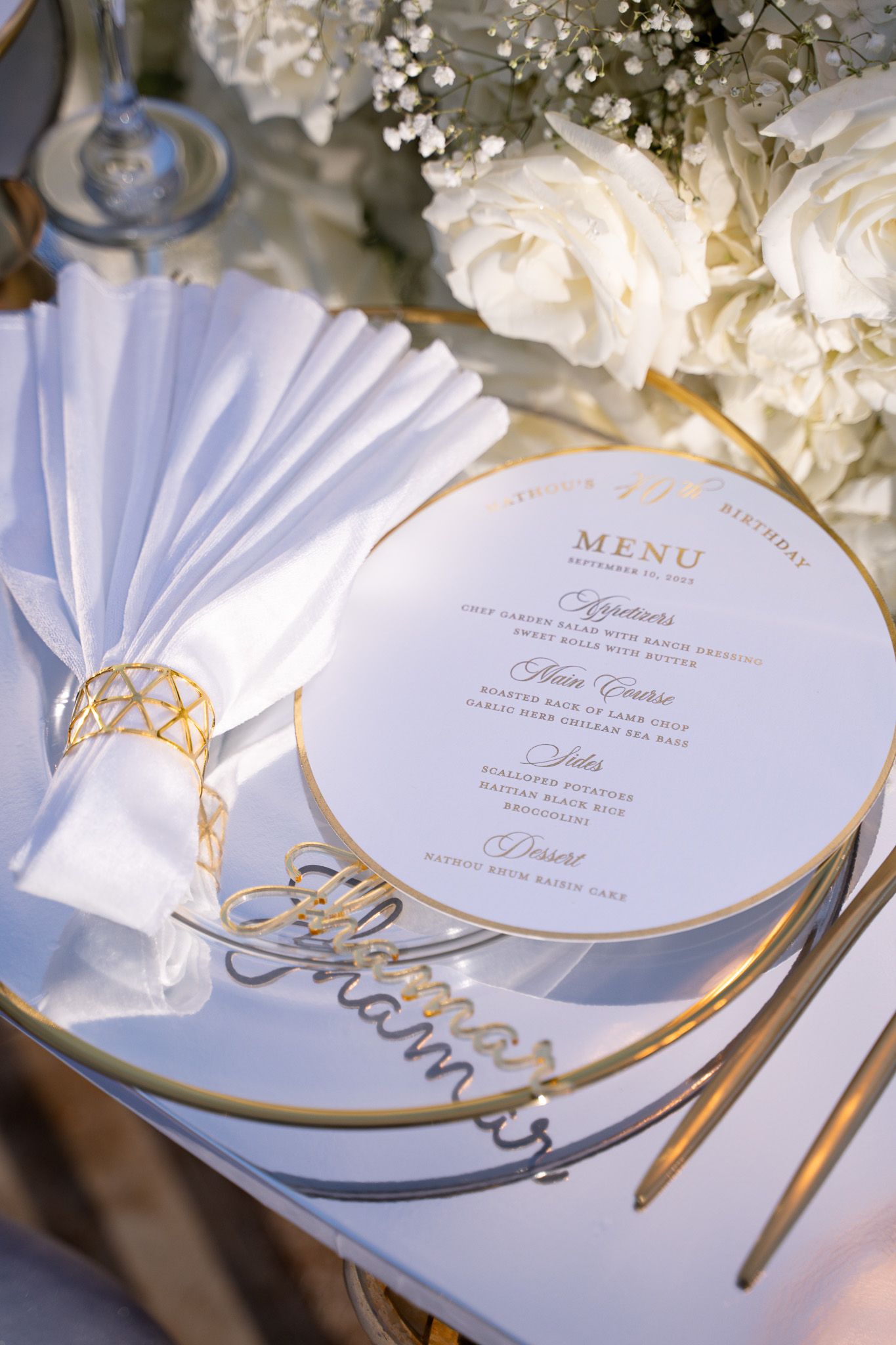 Elegant wedding menu card with gold trim beside white roses and fan-folded napkin.