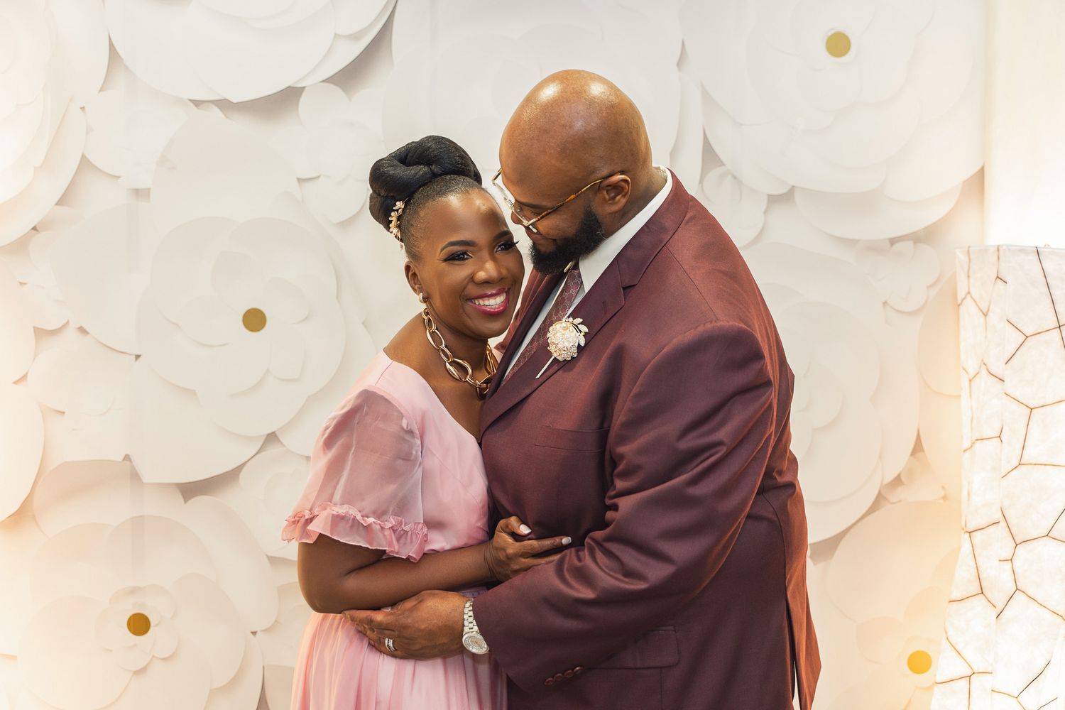 A romantic moment between newlyweds sharing laughter against a white decorative backdrop.