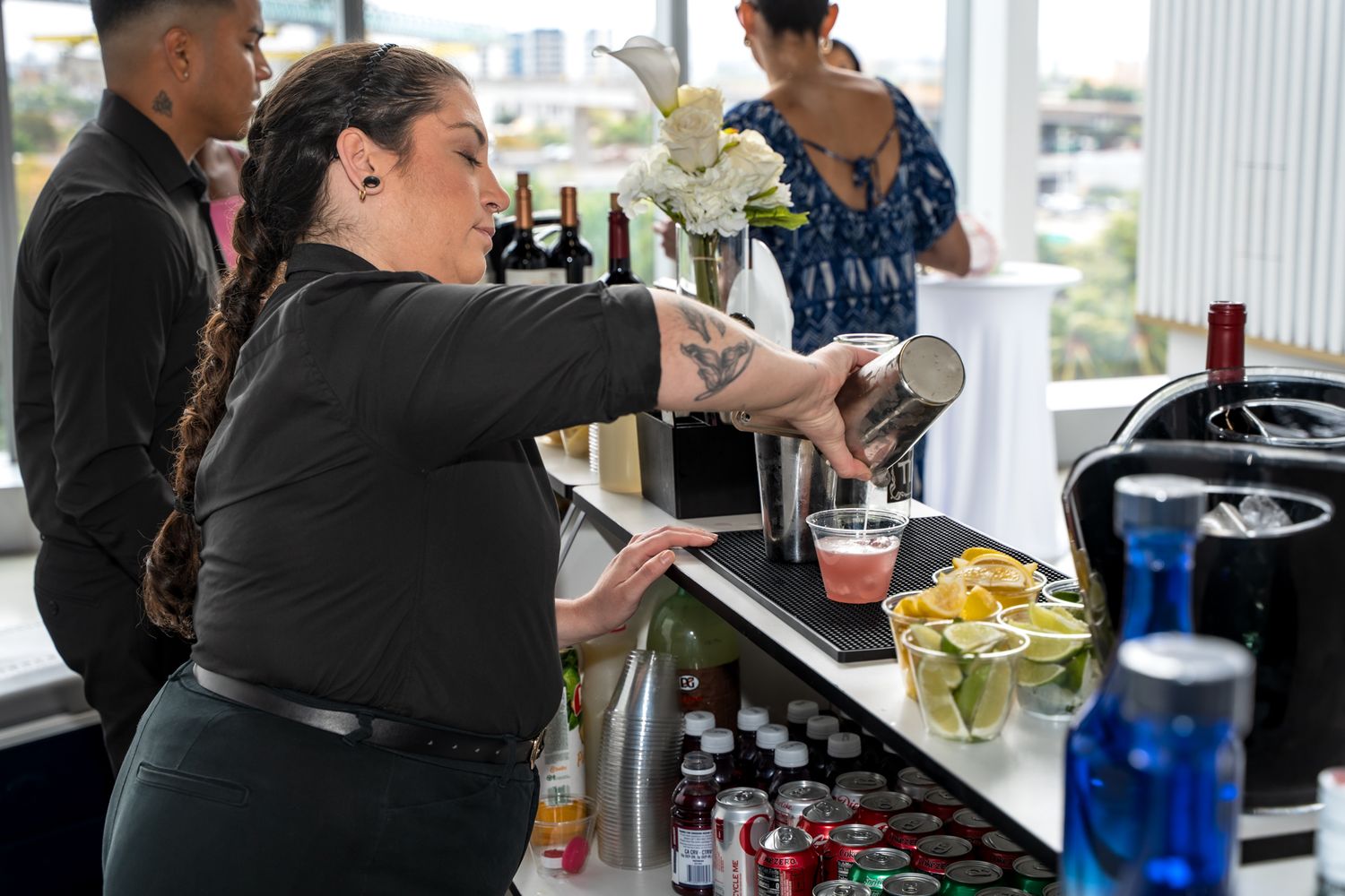 Bartender preparing drinks at an event bar with various bottles and mixers.