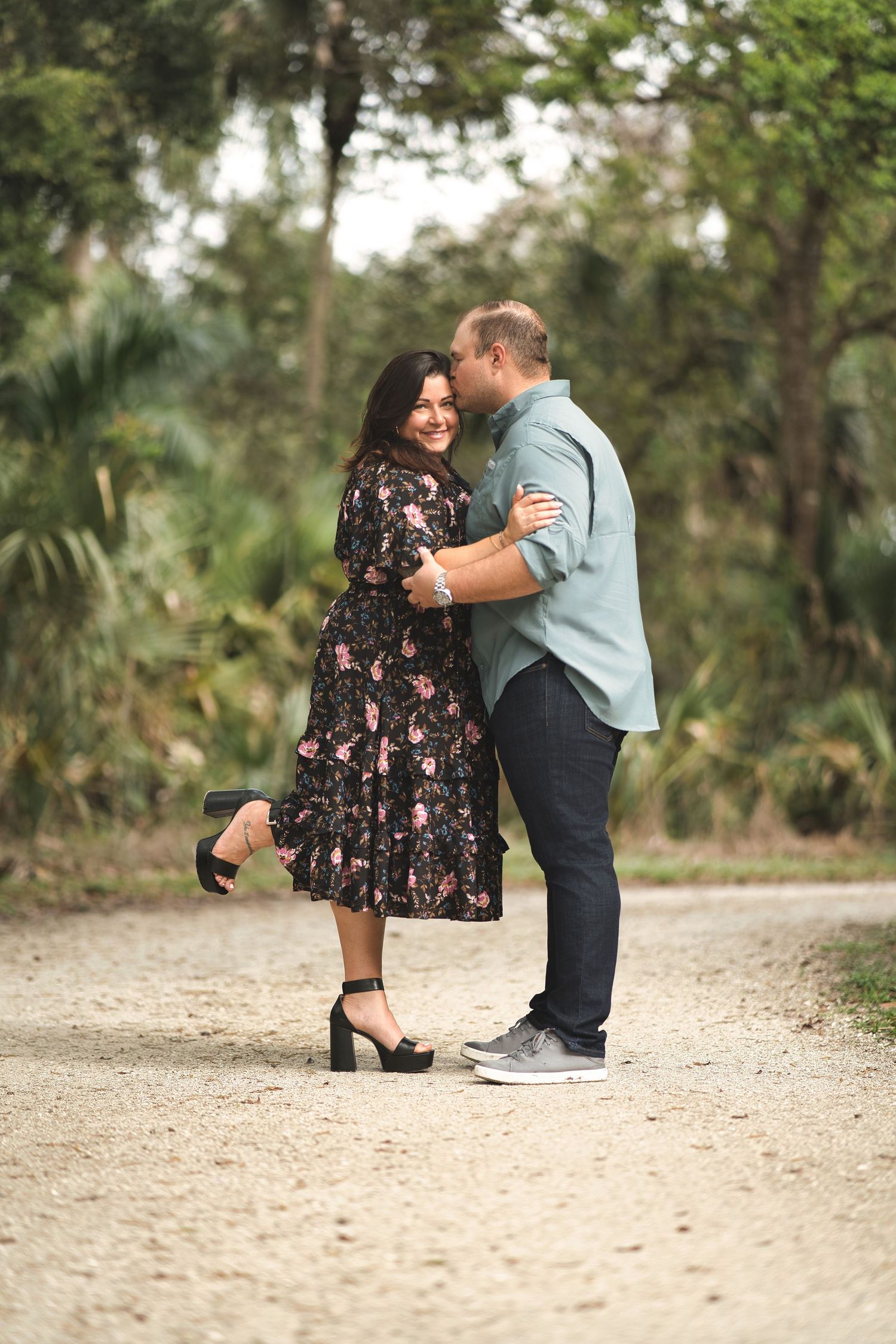 Romantic couple embracing on a dirt path surrounded by palm trees.