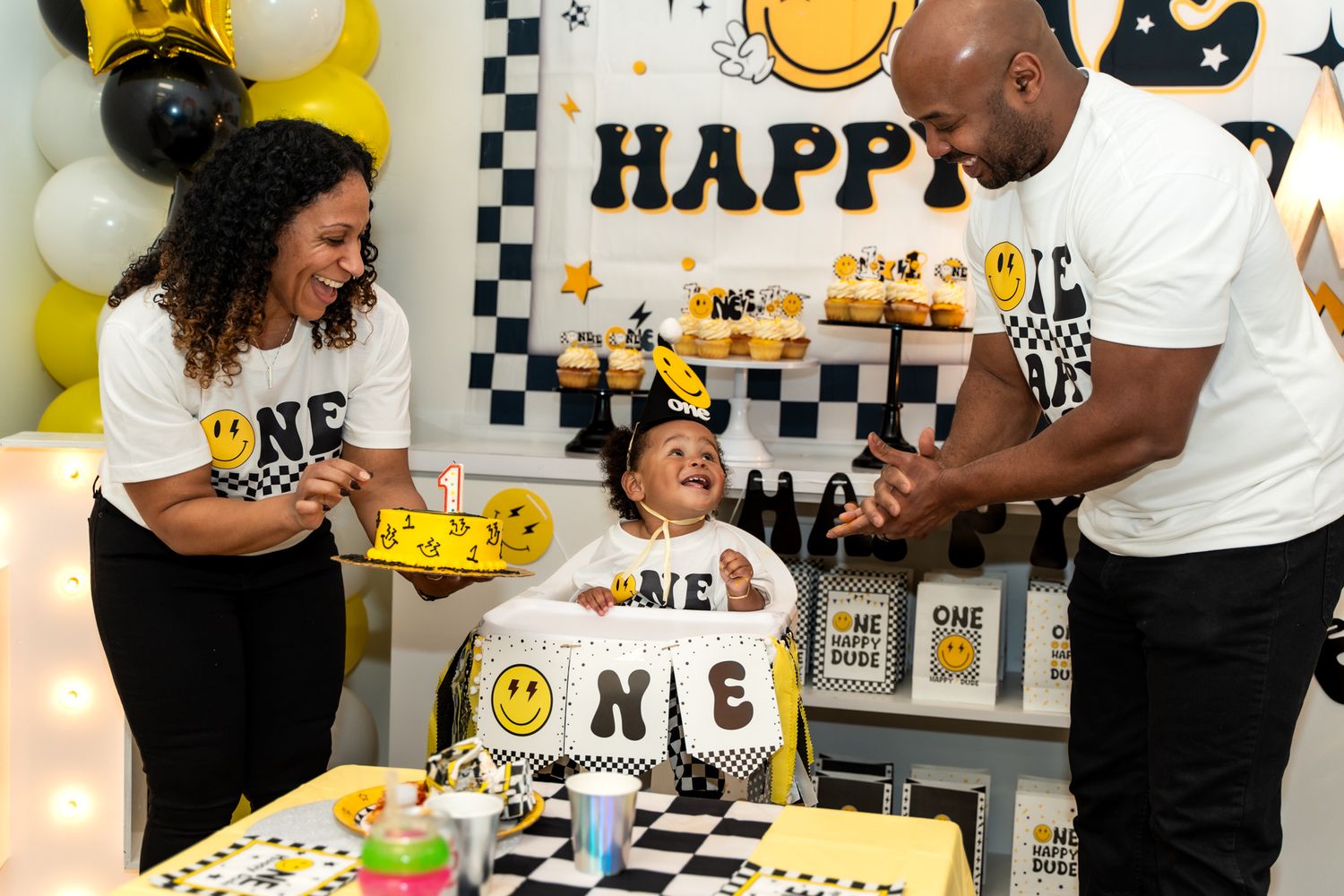Birthday party celebration with a smiley face themed cake and decorations in yellow and black colors.