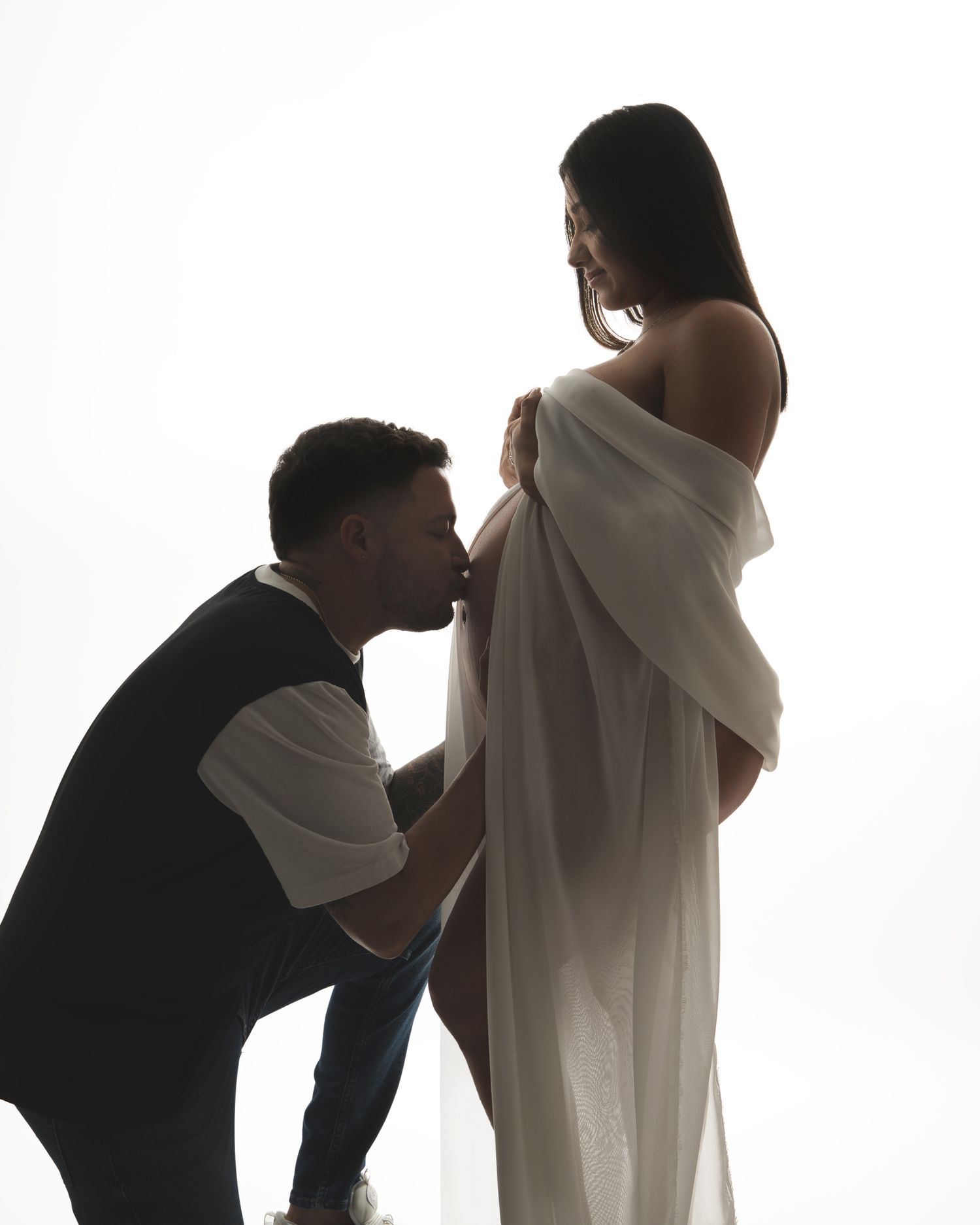 Silhouette maternity photo with couple sharing intimate moment against white background.