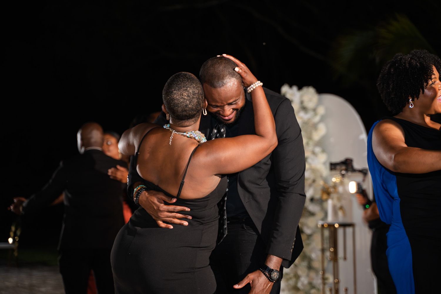 Couples dancing together at an evening wedding reception celebration with floral decor in background.