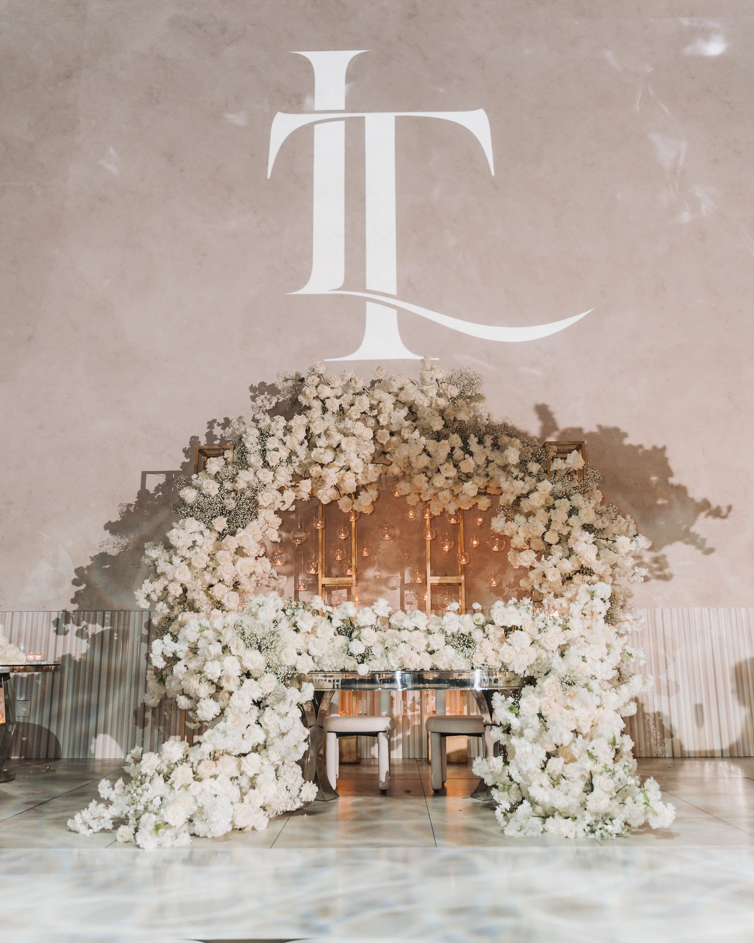 Elegant wedding altar featuring white floral arch and monogram design against neutral backdrop.