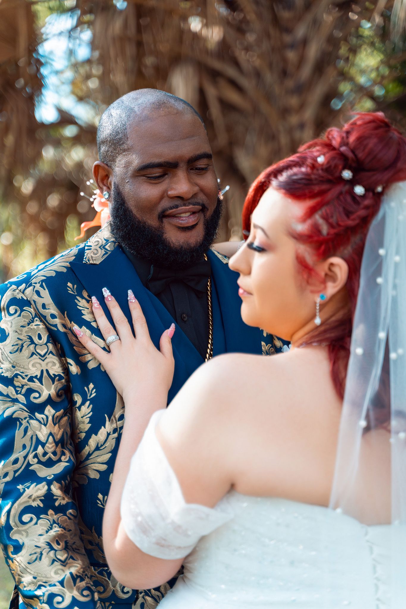 A loving couple in wedding attire embracing outdoors with palm trees in background.