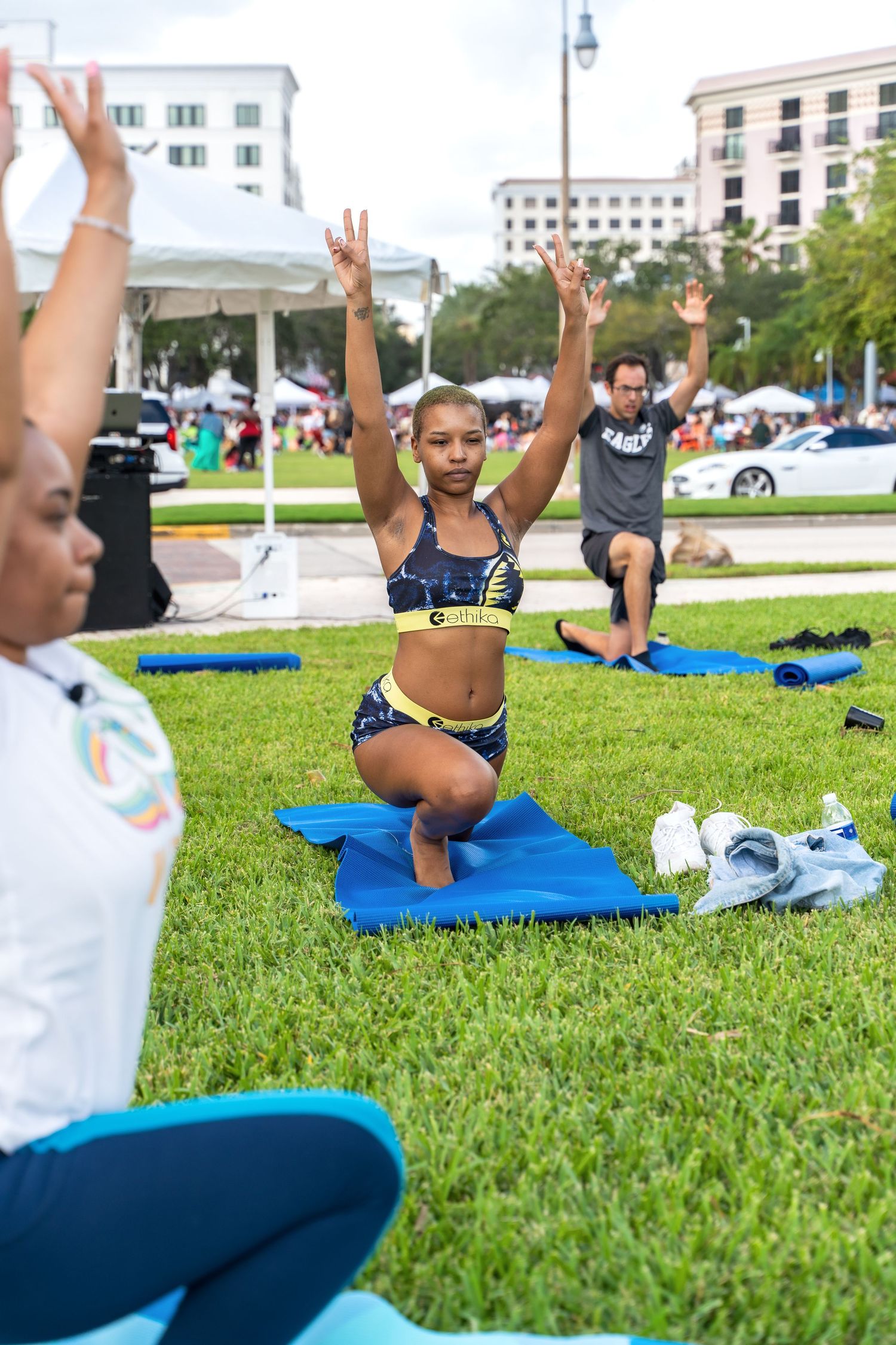 Outdoor fitness class participants doing squats on blue yoga mats in an urban park setting.