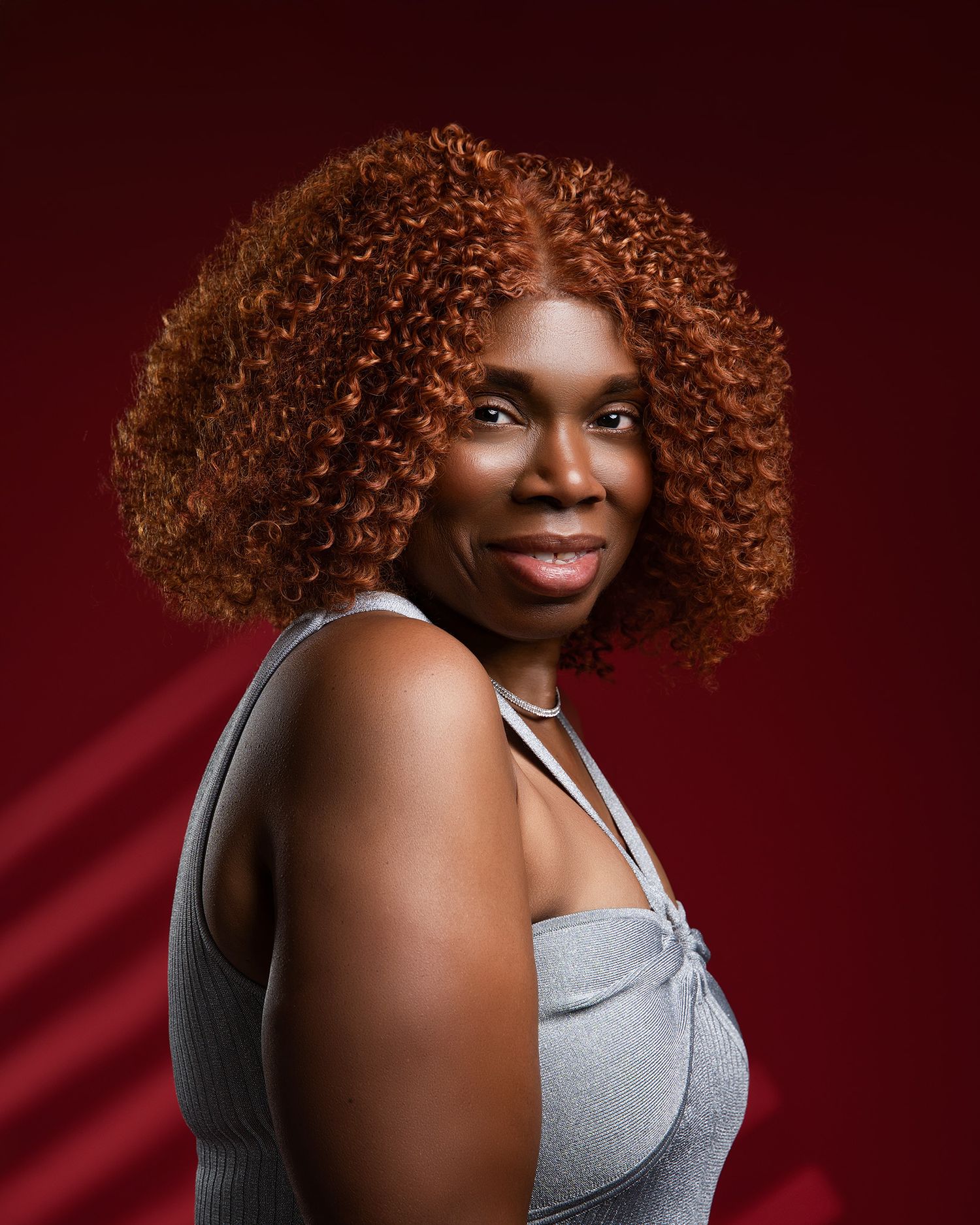 Close-up portrait against red background featuring natural curly hairstyle.