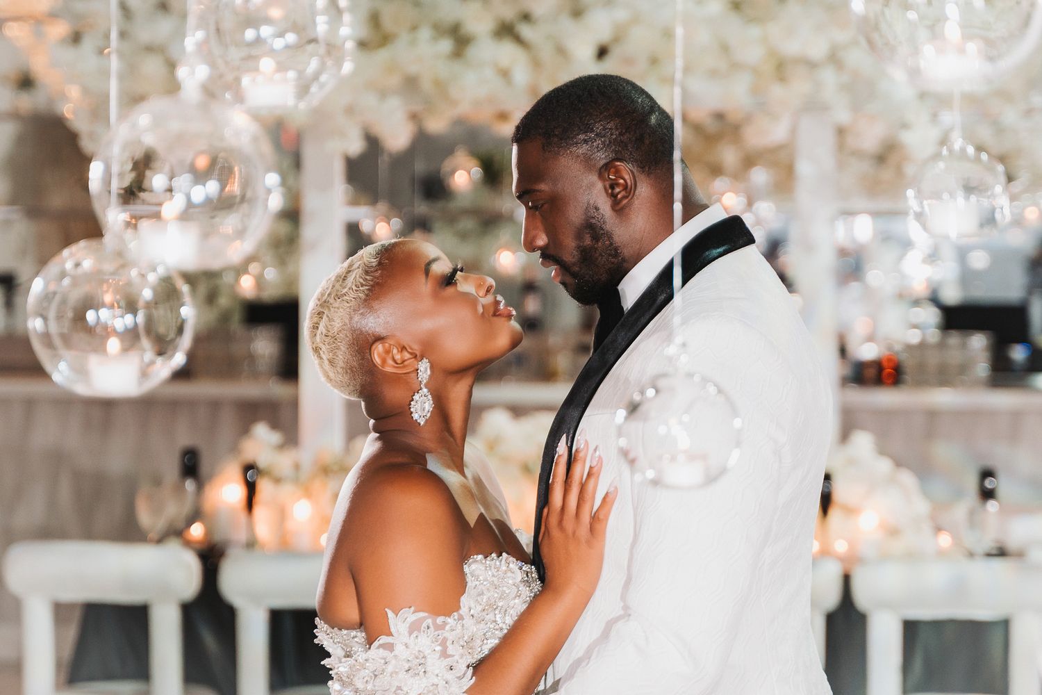 An intimate moment between a couple in wedding attire beneath hanging glass orb decorations.