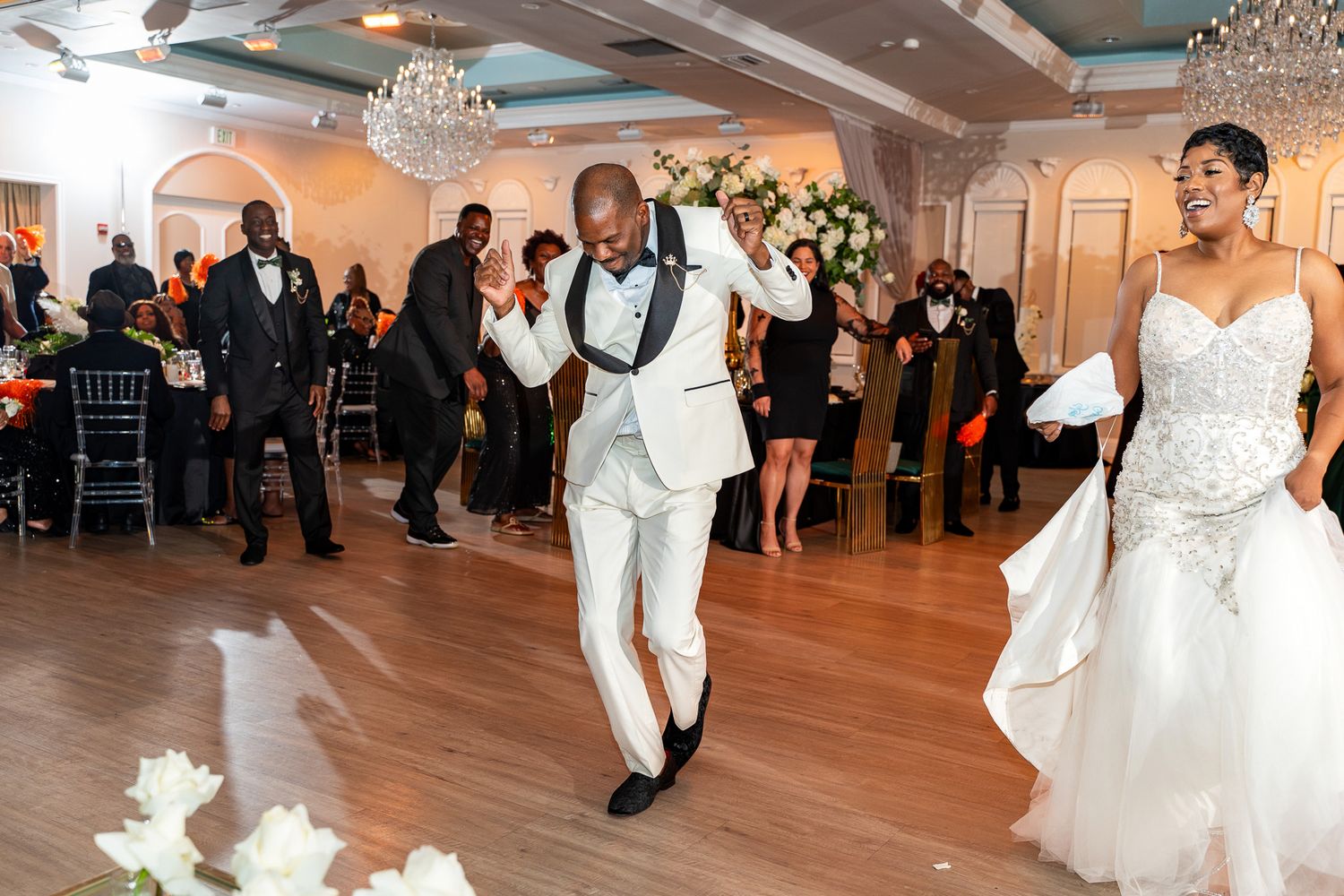 Couple dances joyfully in a ballroom while wedding guests look on from their tables.