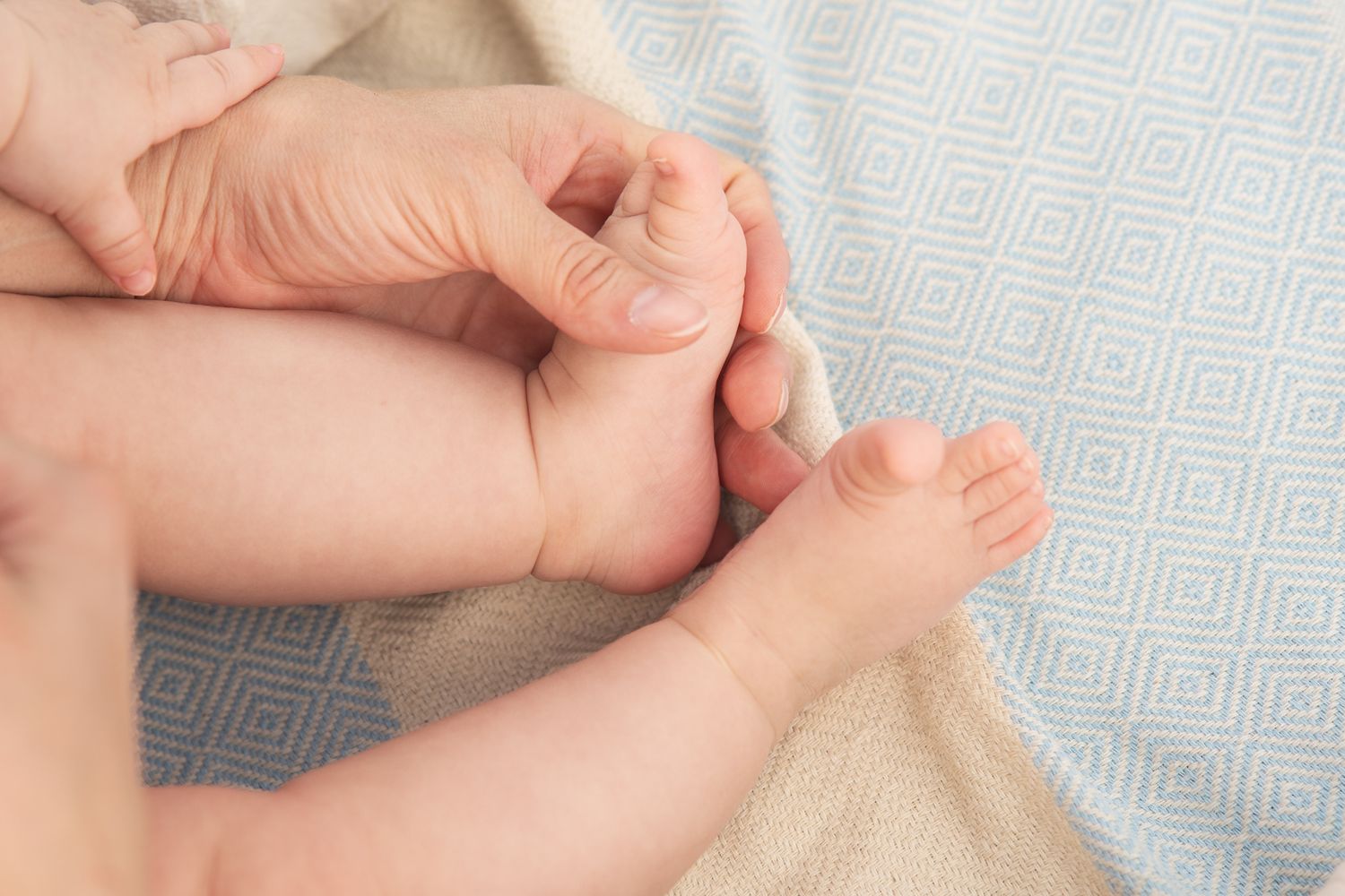 Close up of tiny baby feet and hands being held gently on a textured blanket.