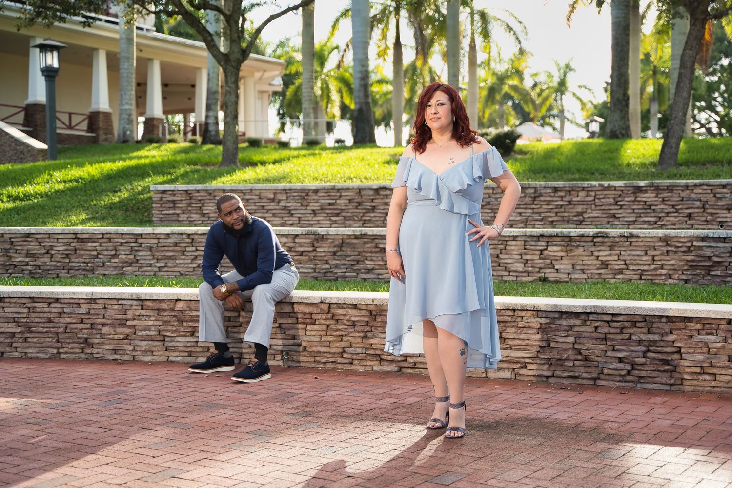 A couple poses separately on stone steps in a lush garden setting with palm trees.