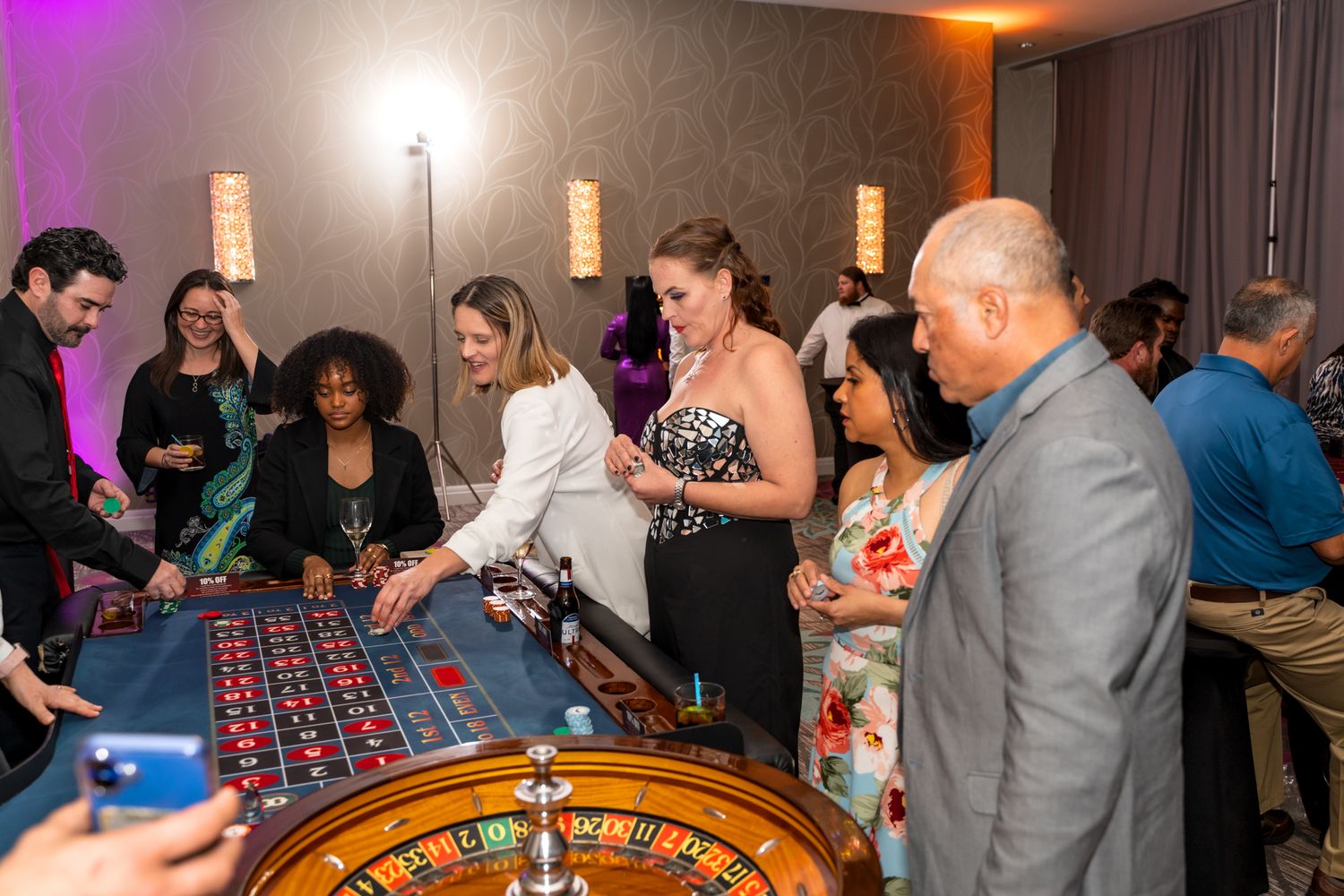 Casino party guests gathered around a roulette table with atmospheric lighting.