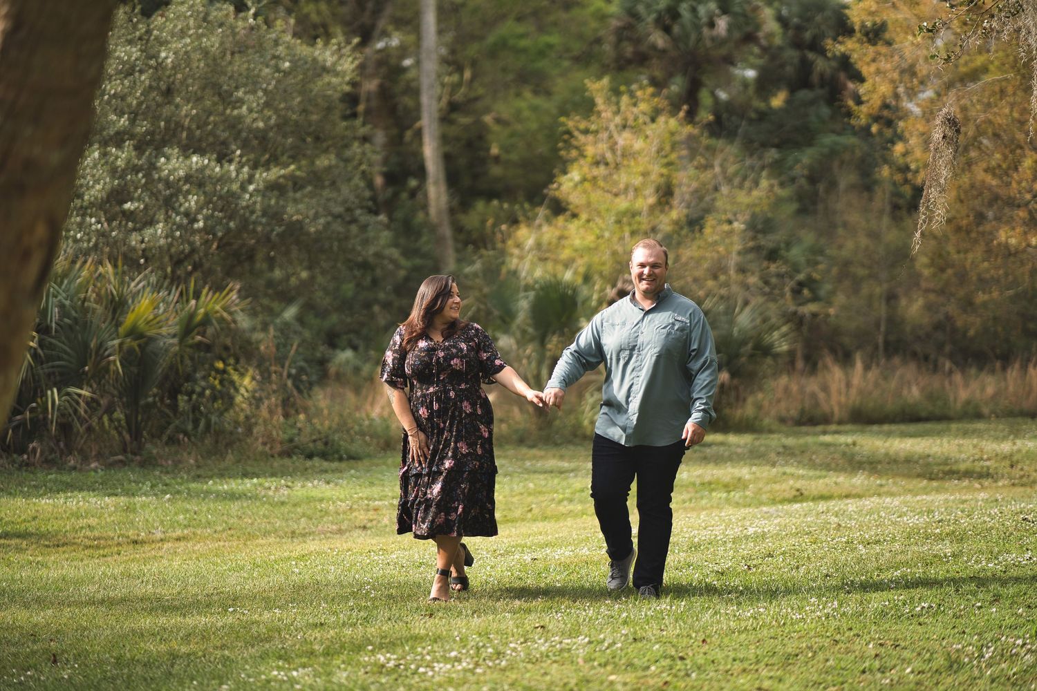 Two people walking together on green grass with trees in background.