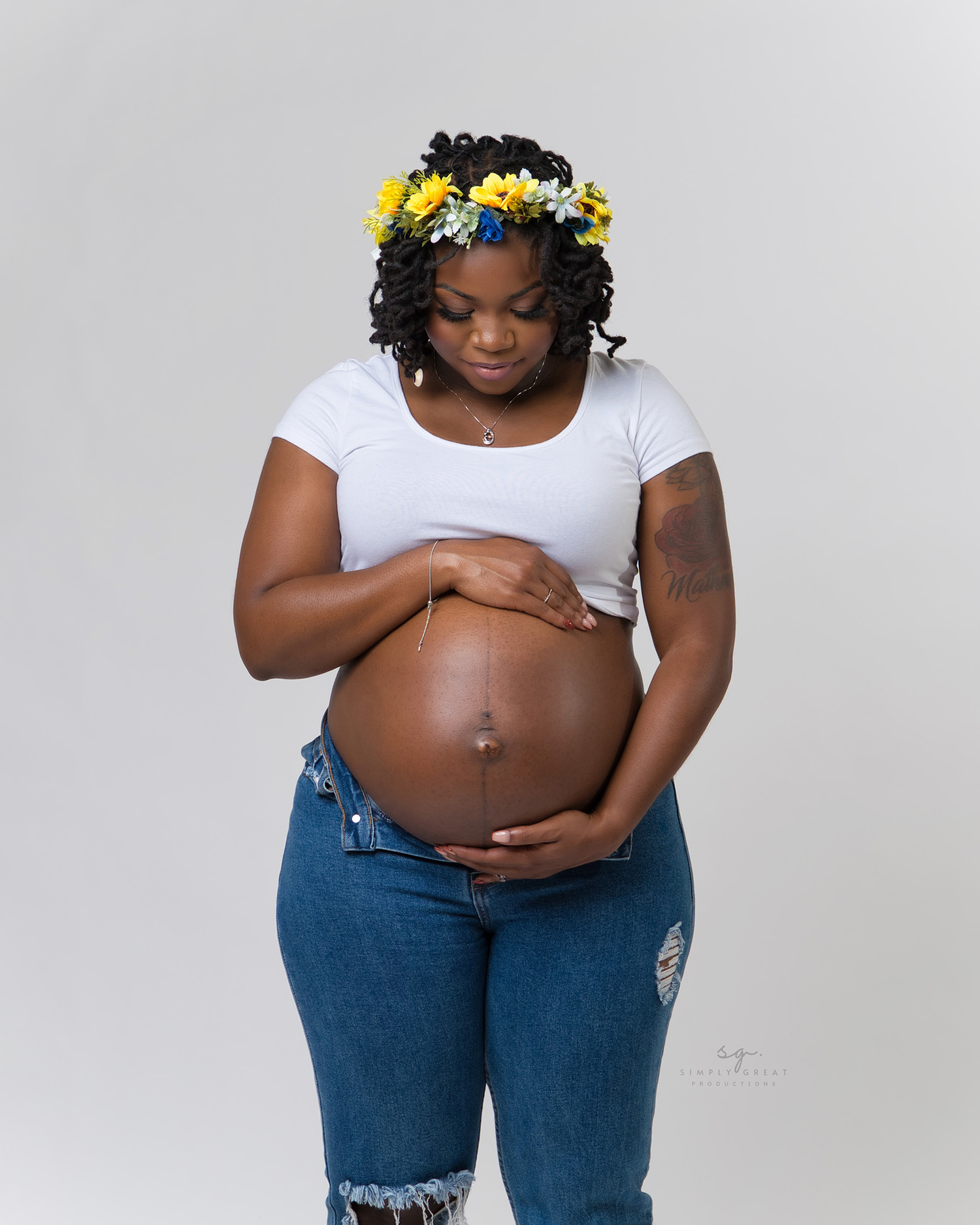 Expectant mother wearing floral crown and white top lovingly cradles her baby bump.