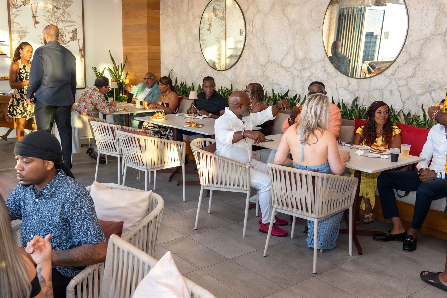 Diners seated at tables in a modern restaurant with round mirrors and woven chairs during a busy service period.