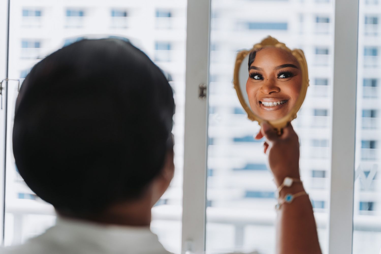 Reflection of bride getting ready in window with cityscape background.