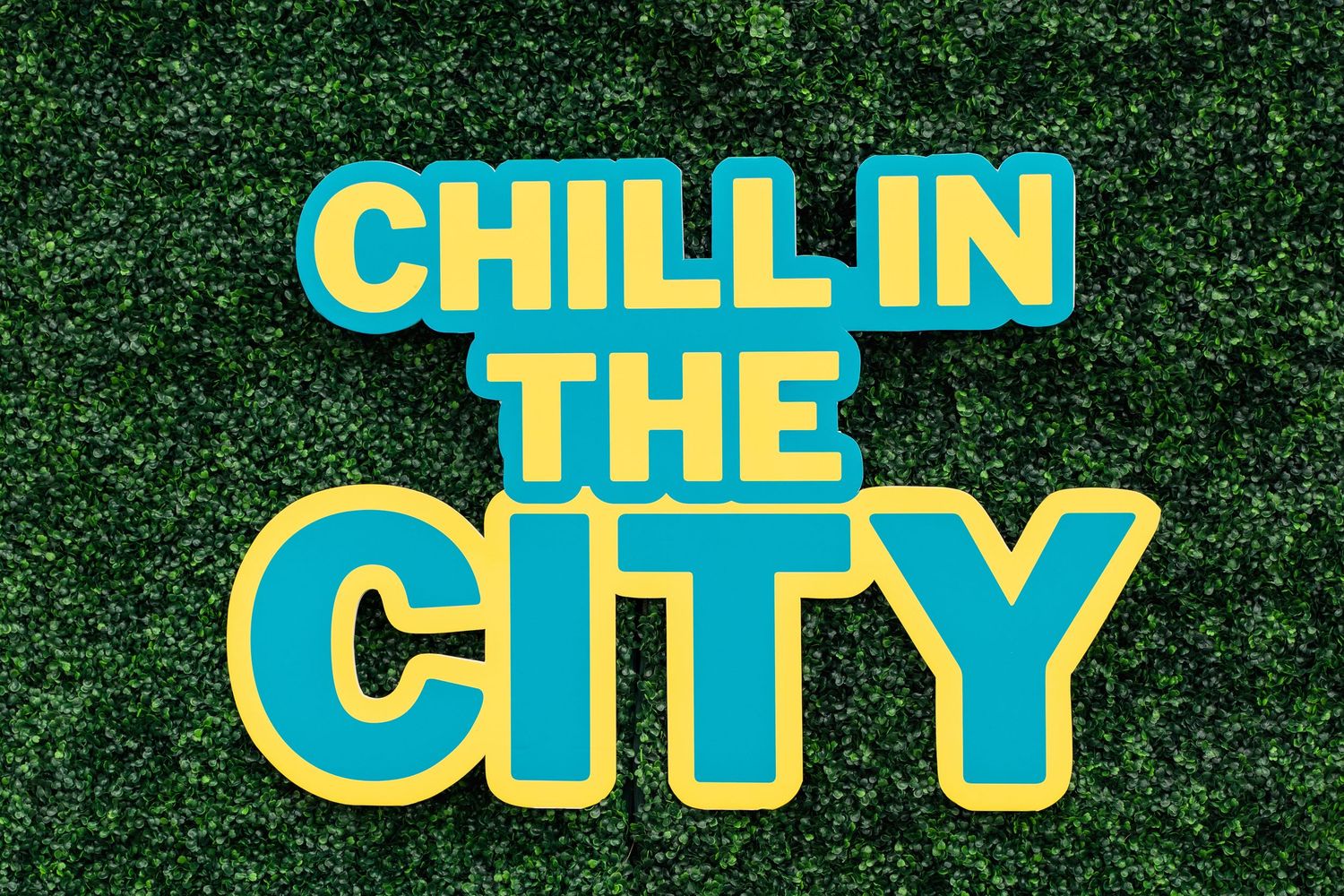 Teal and yellow 'Chill in the City' text against green hedge background.
