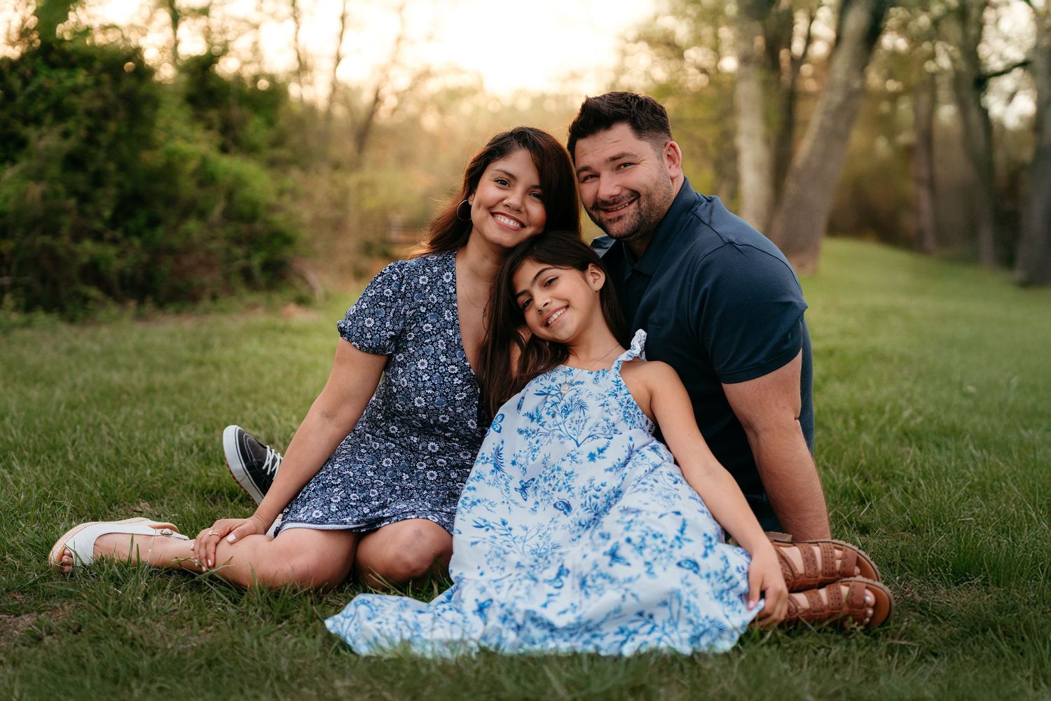 A family sits together on grass during golden hour wearing coordinating blue outfits.