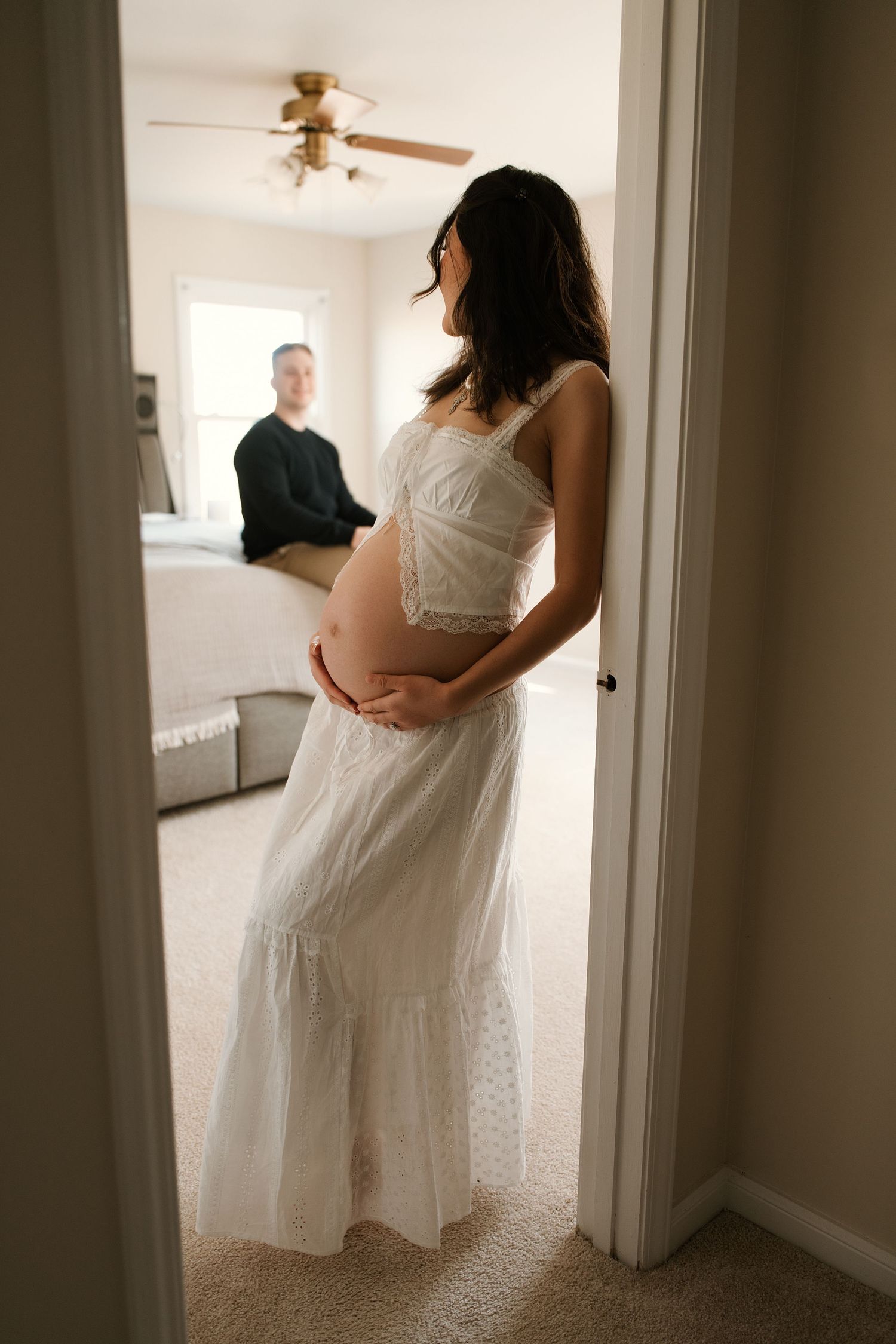 A series of intimate maternity photos showing a person in a white dress standing in a sunlit room.
