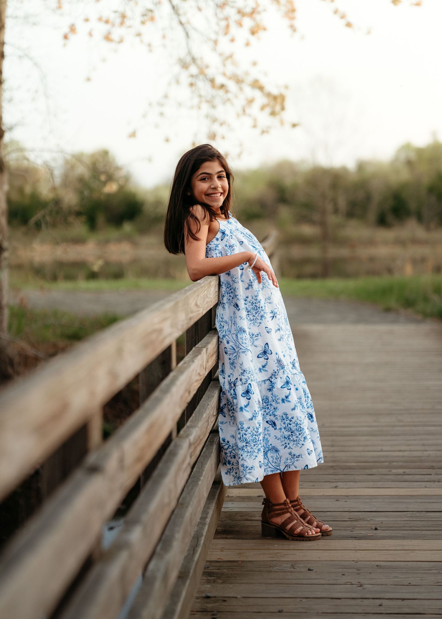 young woman in a blue floral dress sitting and posing on a wooden boardwalk in Northern Virginia.