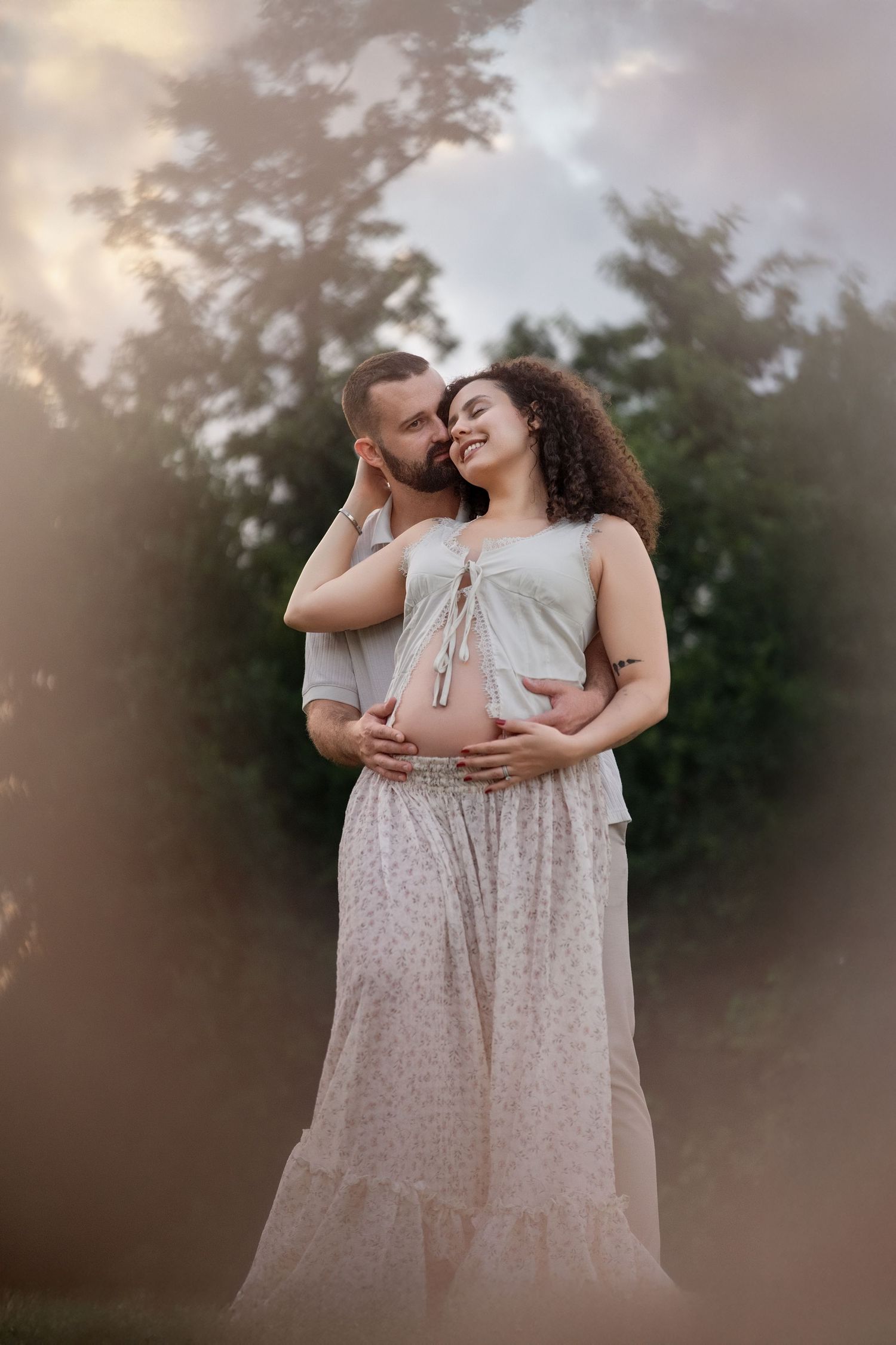 Outdoor maternity session featuring couple in soft lighting and flowy dress.