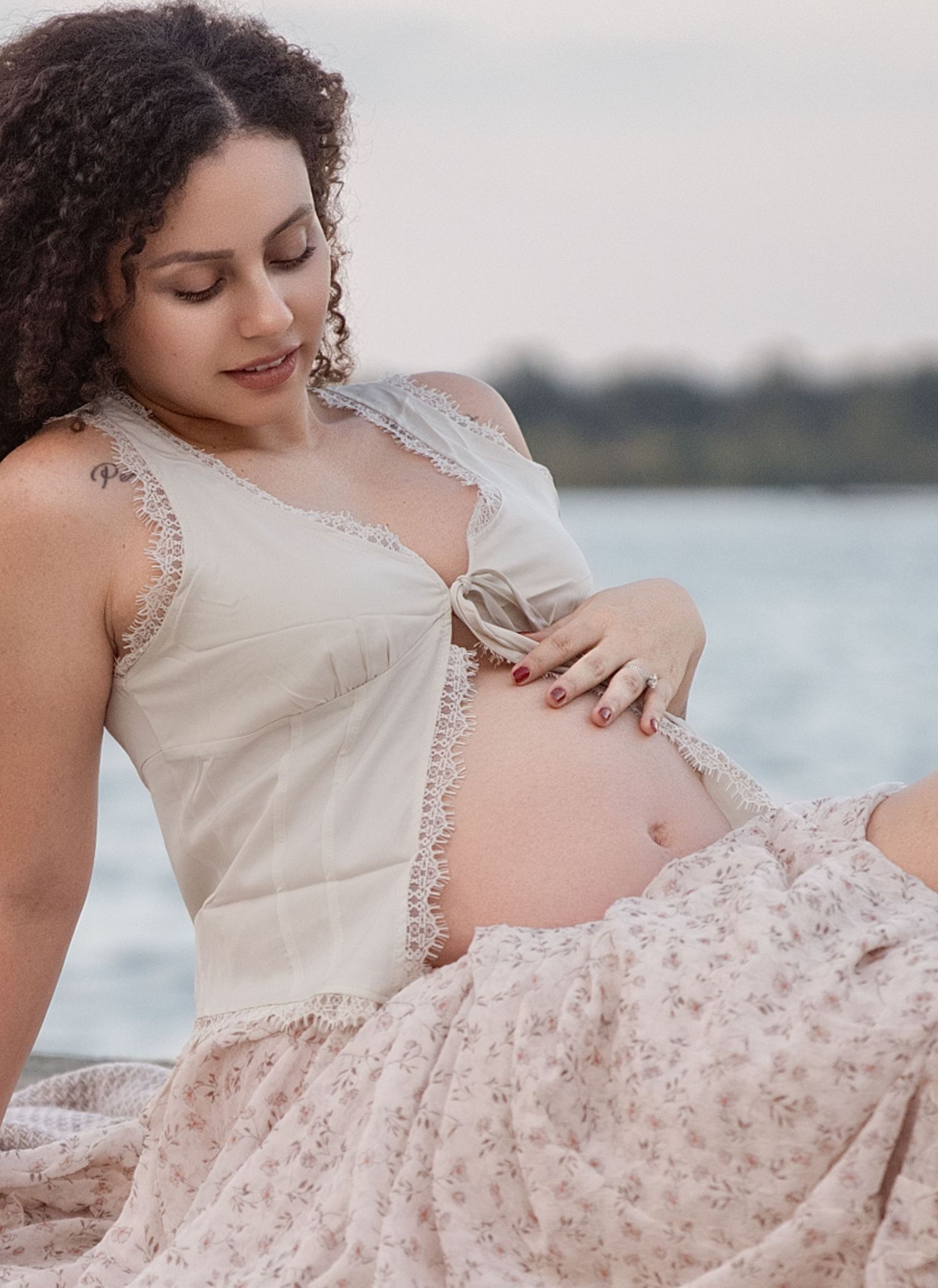 Maternity portrait in blush pink dress by waterfront during sunset.