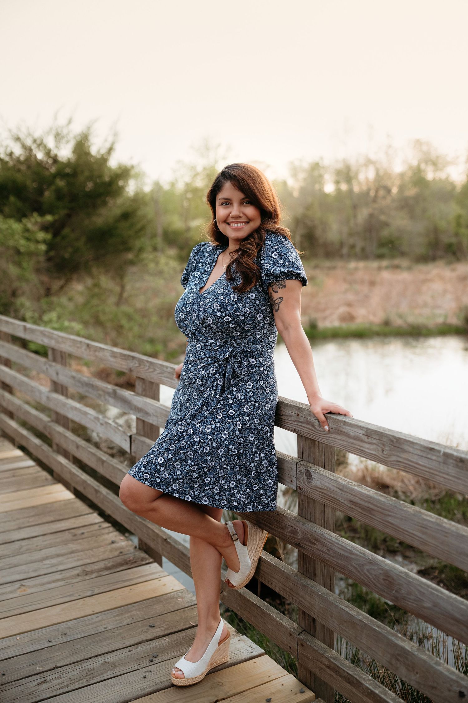 A floral navy blue dress with ruffled sleeves worn on a wooden boardwalk by a lake at sunset.