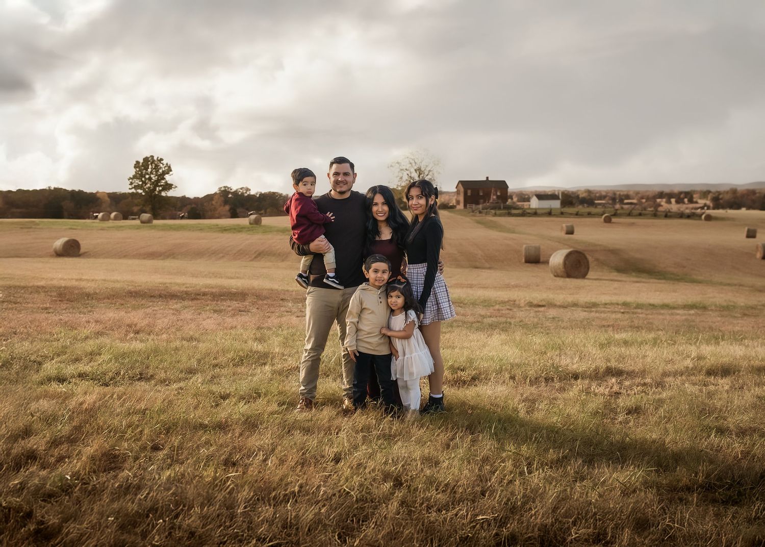 People stand together in a golden prairie field at sunset with hay bales scattered across the landscape.